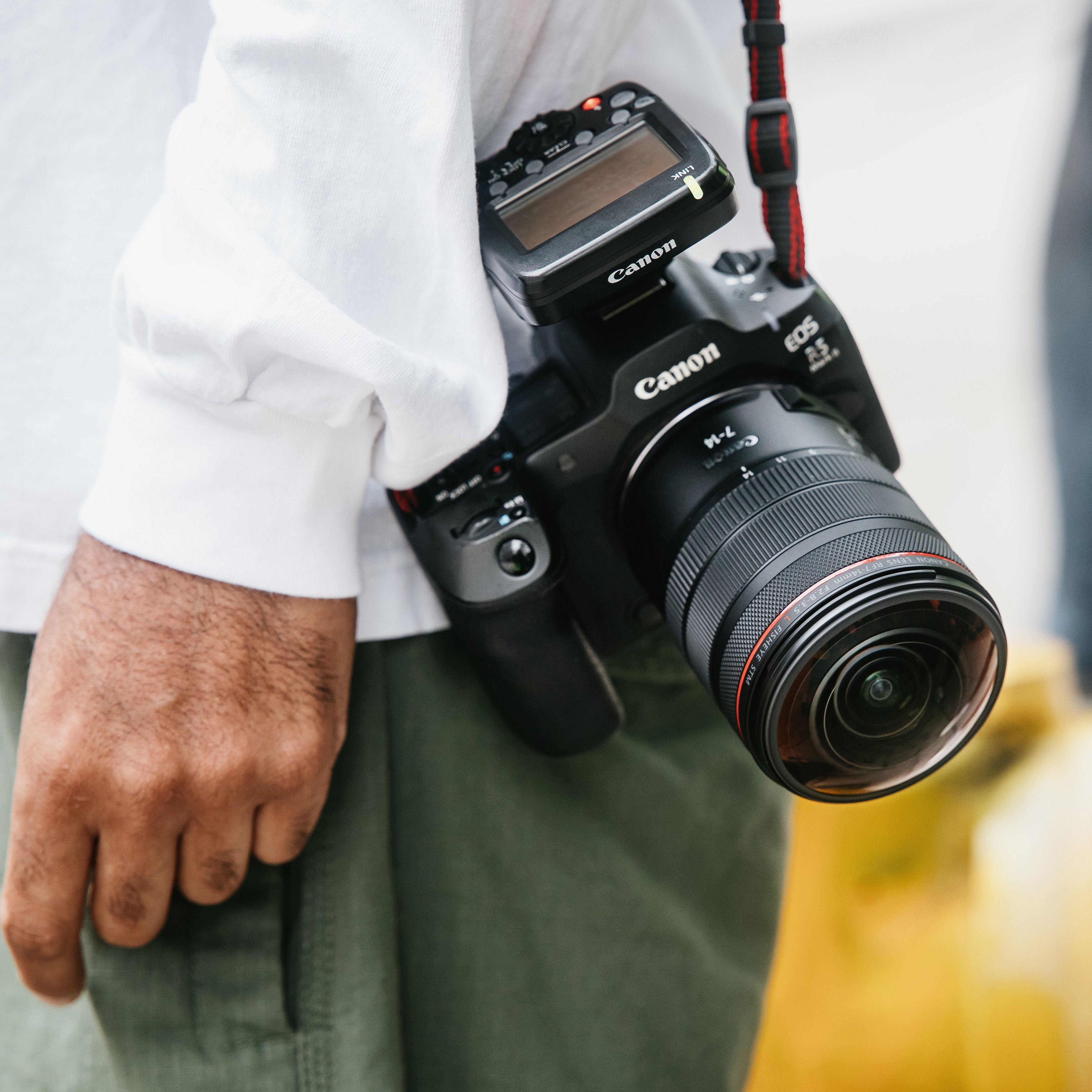 Un appareil photo Canon EOS R5 avec objectif est porté sur une épaule.