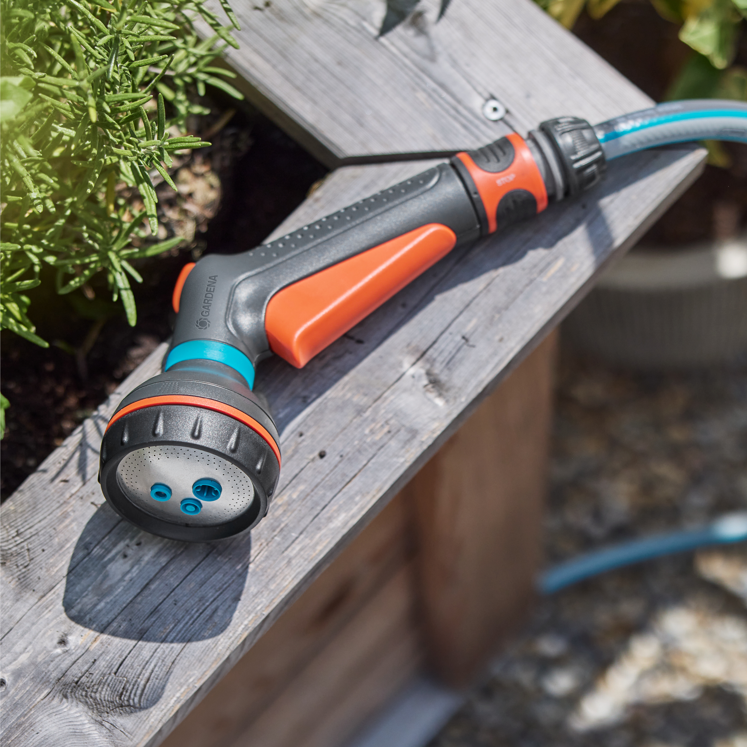 Gartenspritze mit orangefarbenem Griff auf Holzbrett, neben Pflanzen.