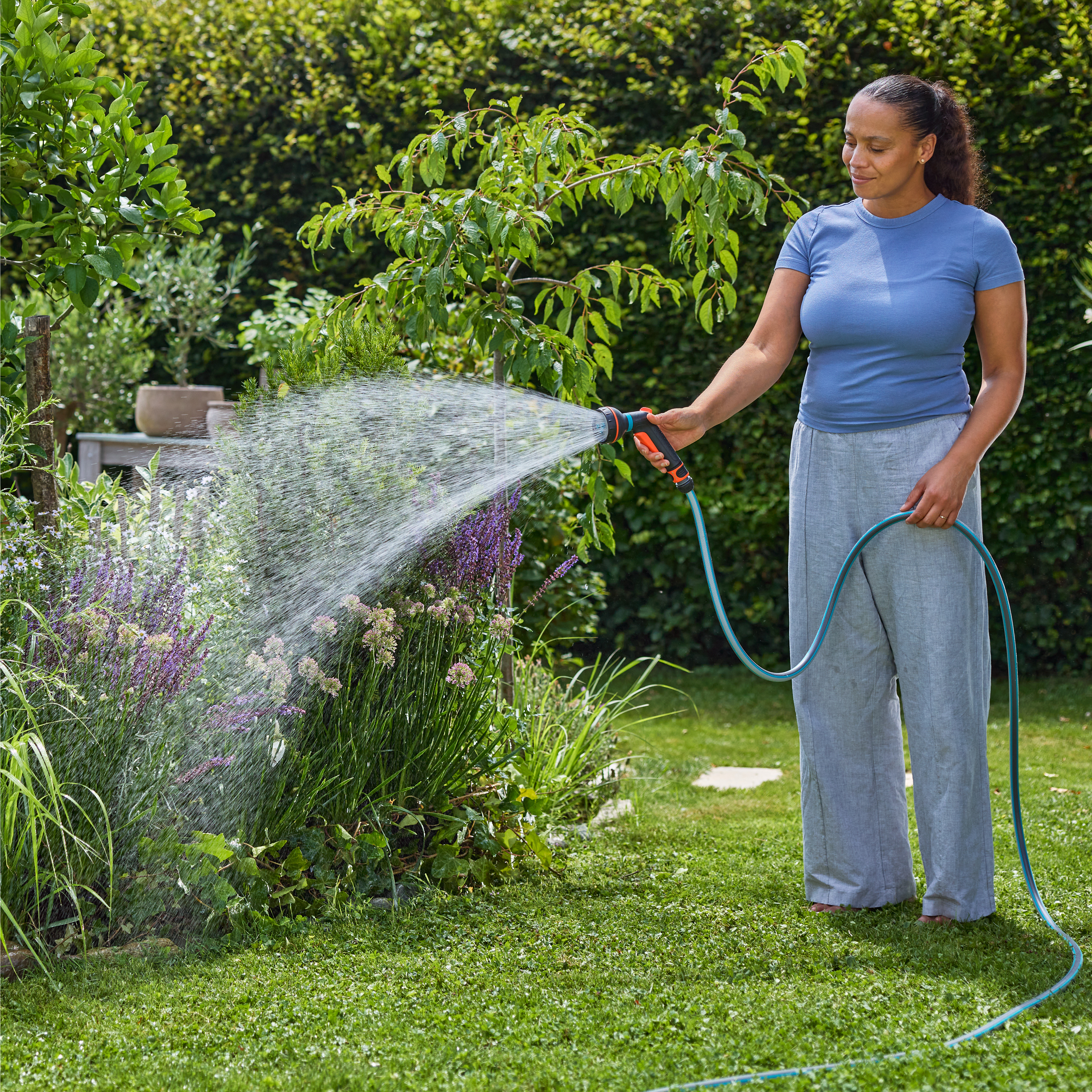 Eine Frau gießt Pflanzen im Garten mit einem Gartenschlauch.