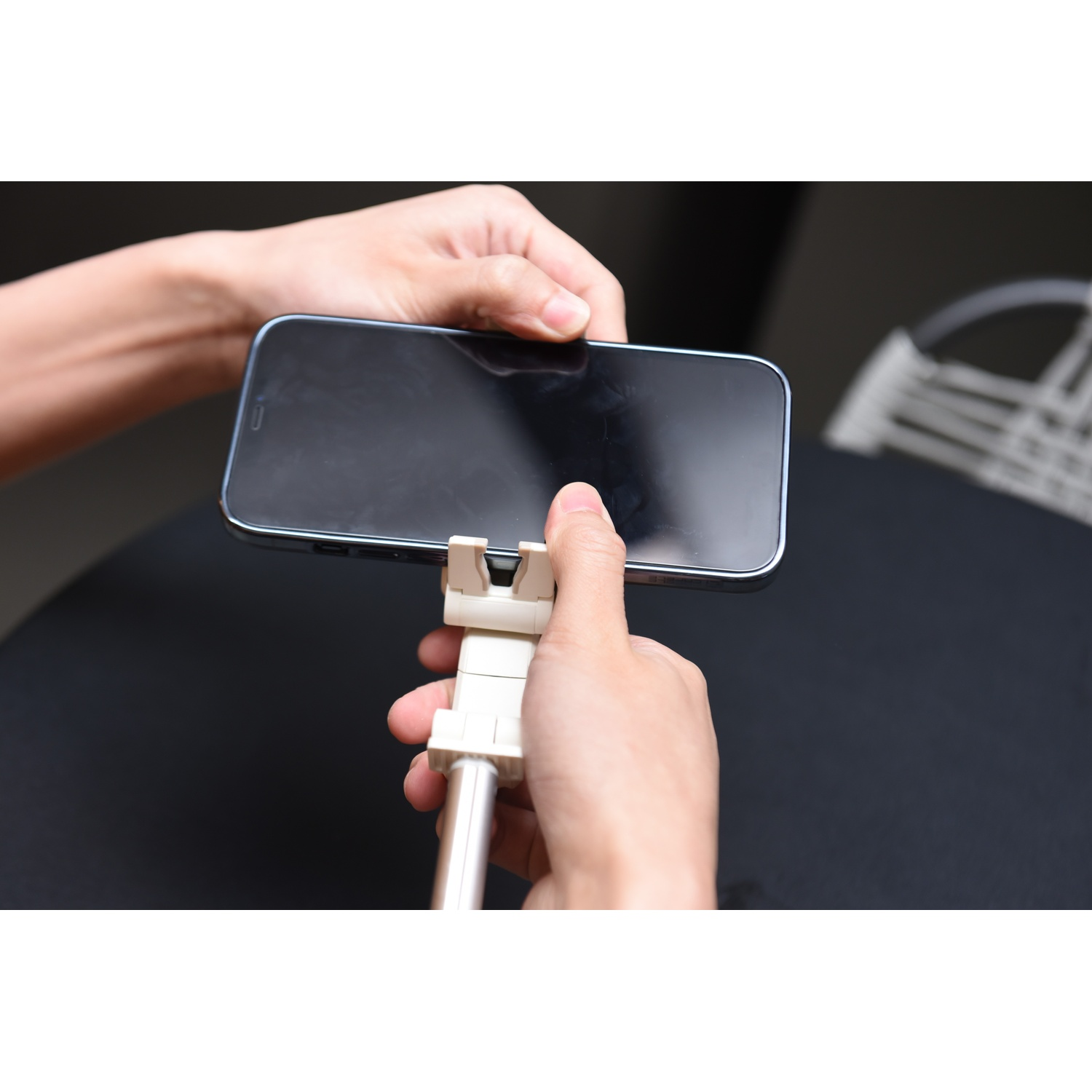 Le mani tengono uno smartphone in un supporto per selfie stick su un tavolo nero.