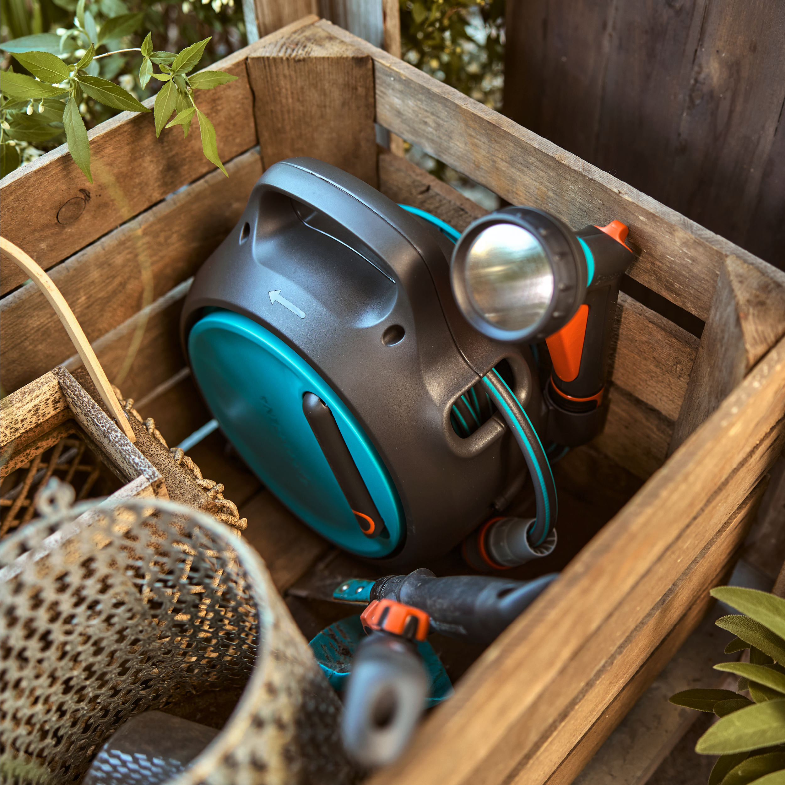 Schwarzer Gartenschlauchaufwickler mit blauem Detail in Holzkiste.