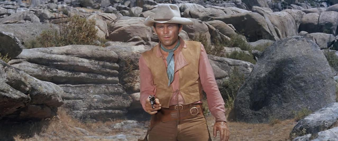 Ein Cowboy mit Hut und Weste hält eine Pistole in felsiger Landschaft.