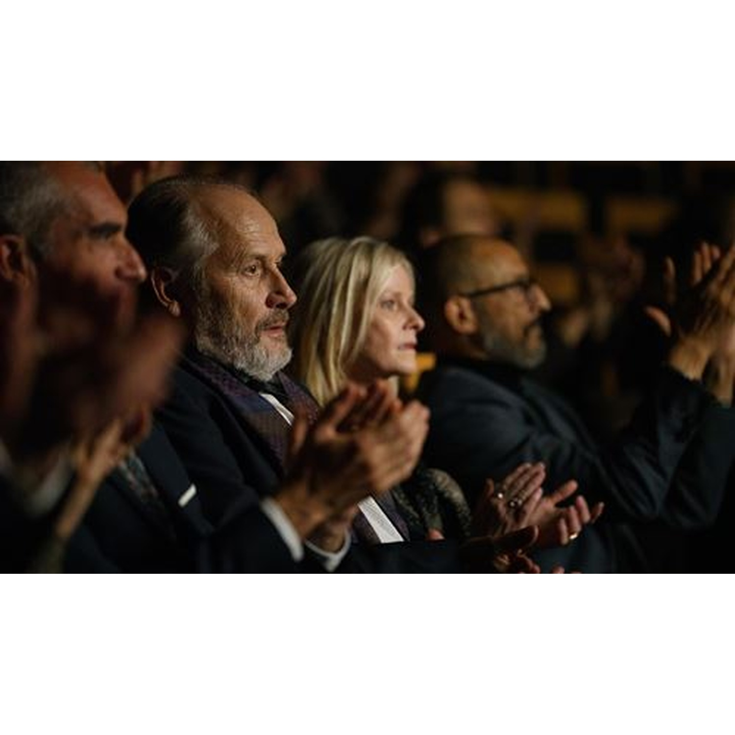 Des gens applaudissent dans une pièce sombre, certains flous au premier plan.