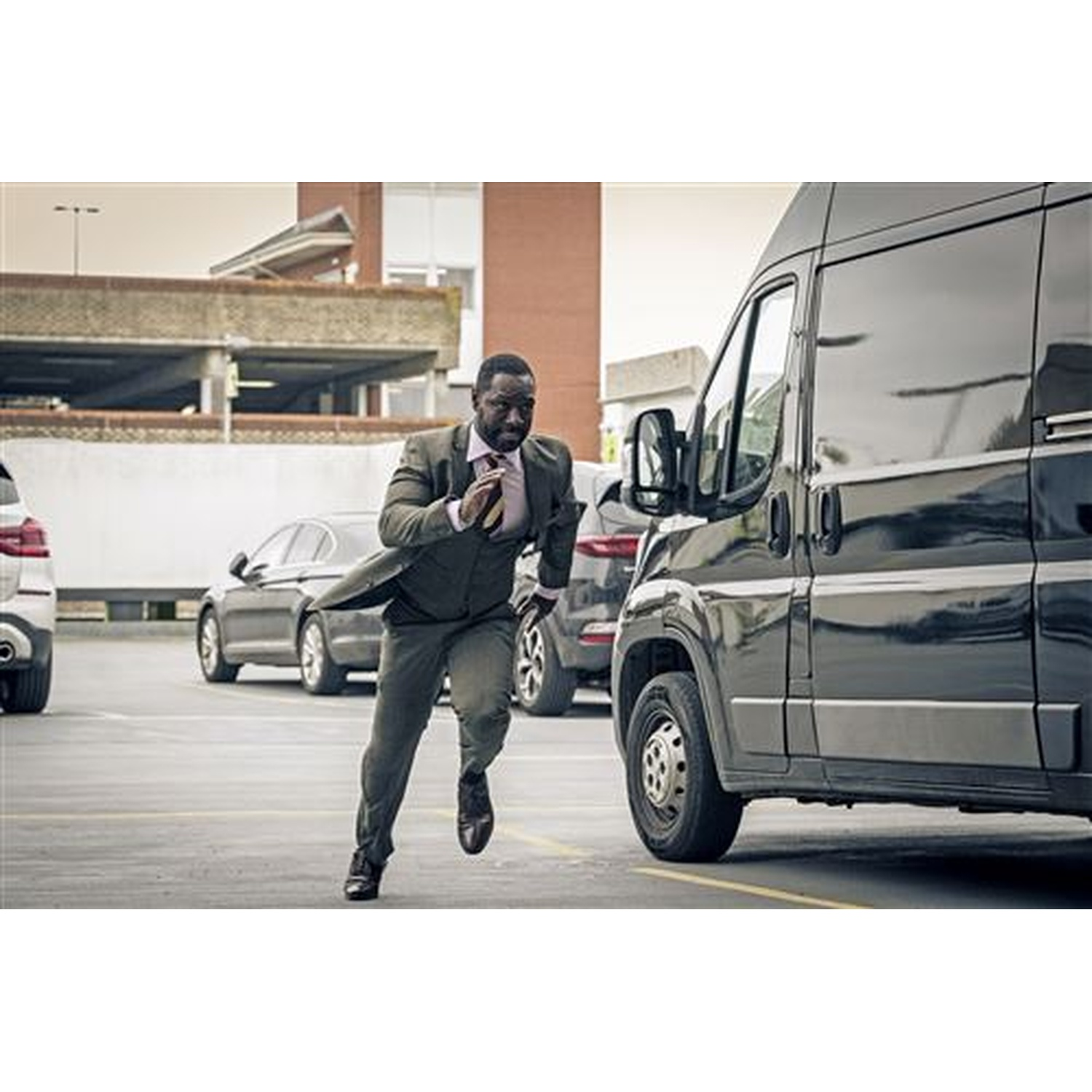 A man in a suit runs in a parking lot next to a black van.