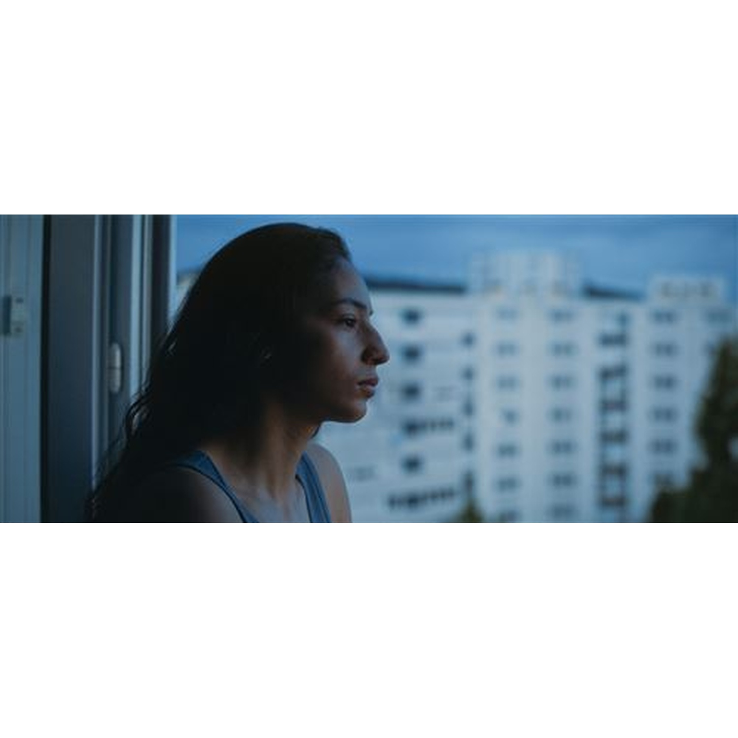Jeune femme regarde pensivement par une fenêtre un bâtiment.