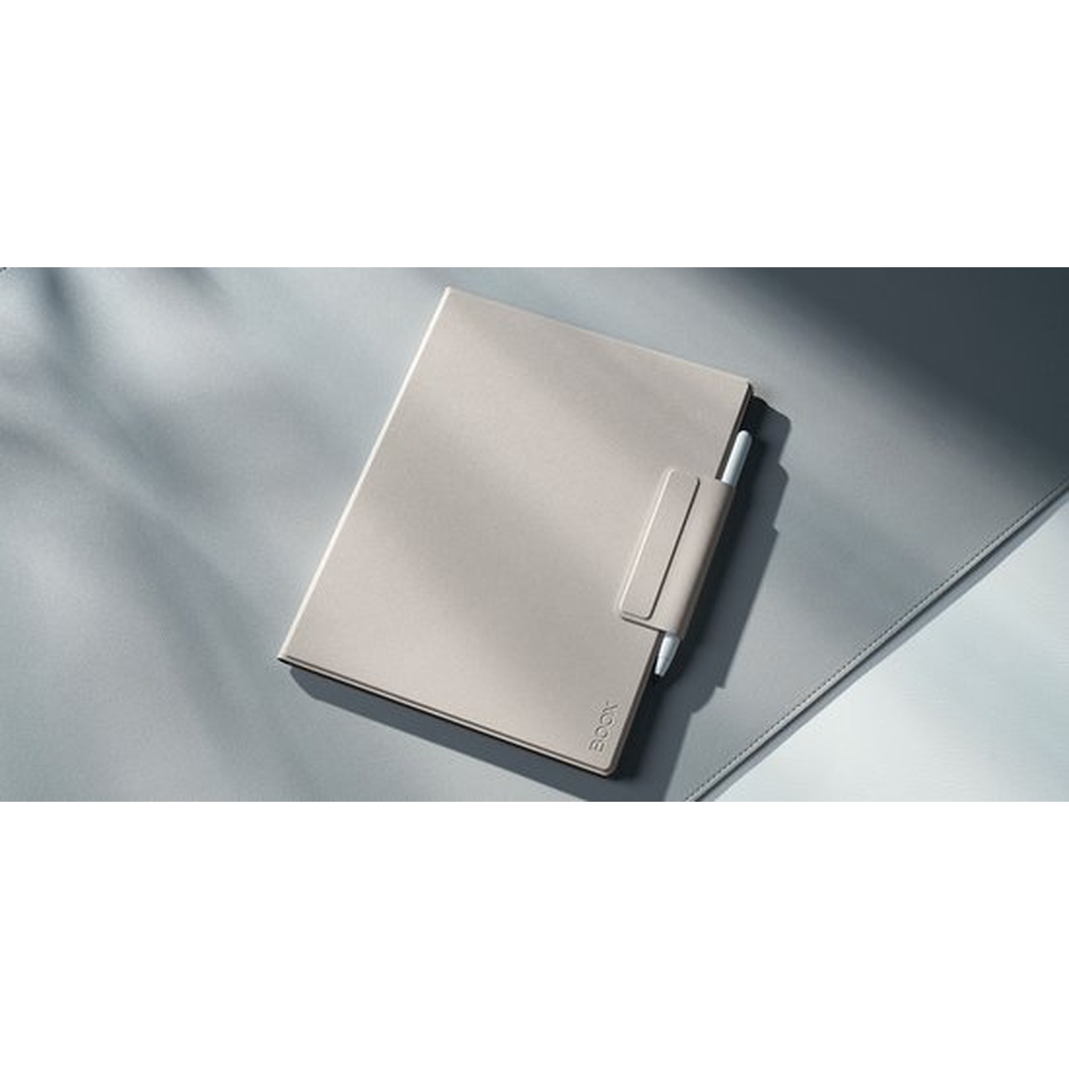 Un carnet beige clair avec porte-stylo et stylo blanc, sur une surface grise.