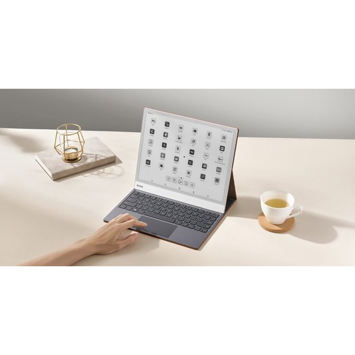 Een hand typt op een laptop met een scherm vol pictogrammen. Een kopje thee ernaast.