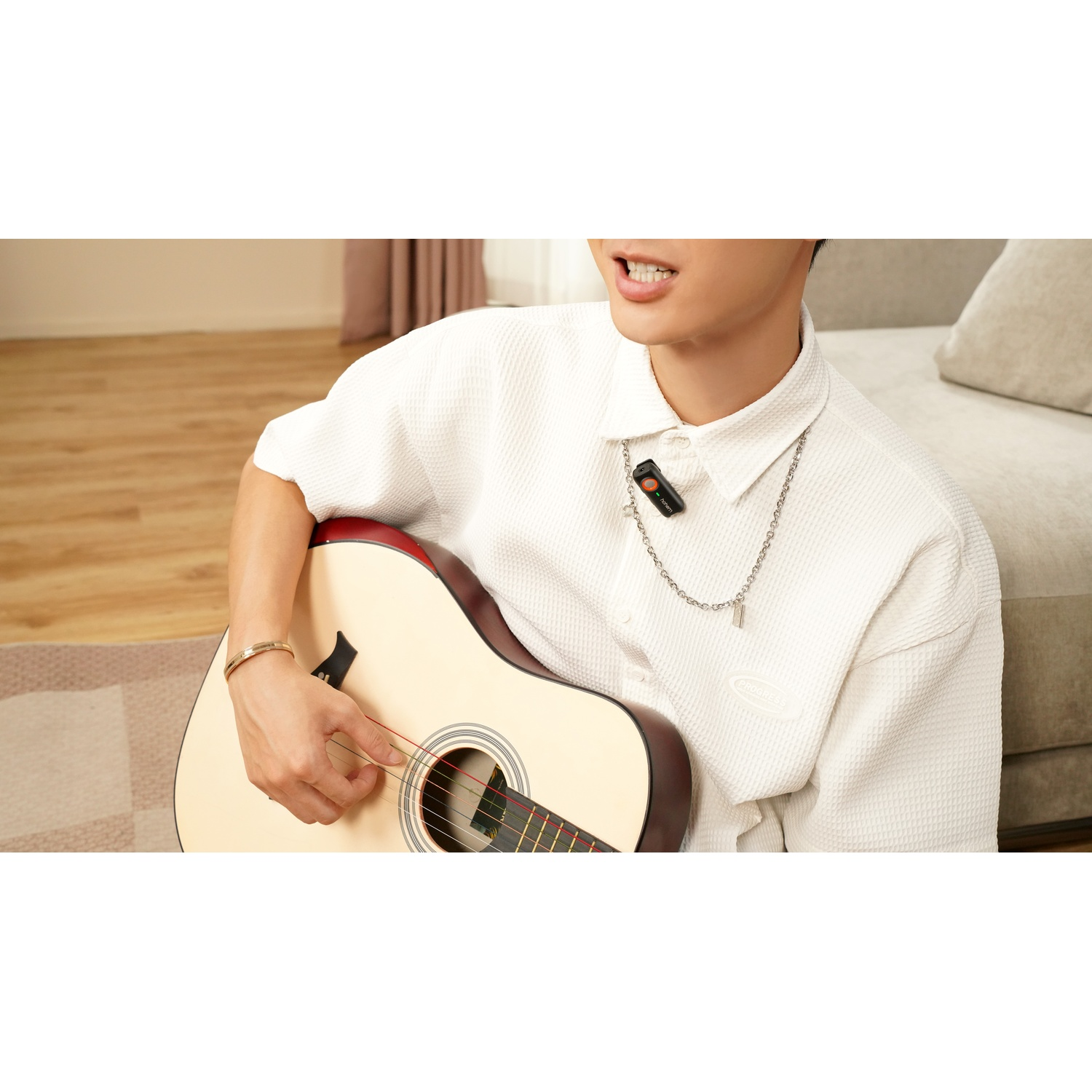 Un uomo suona la chitarra acustica, indossa camicia bianca con microfono al collo.