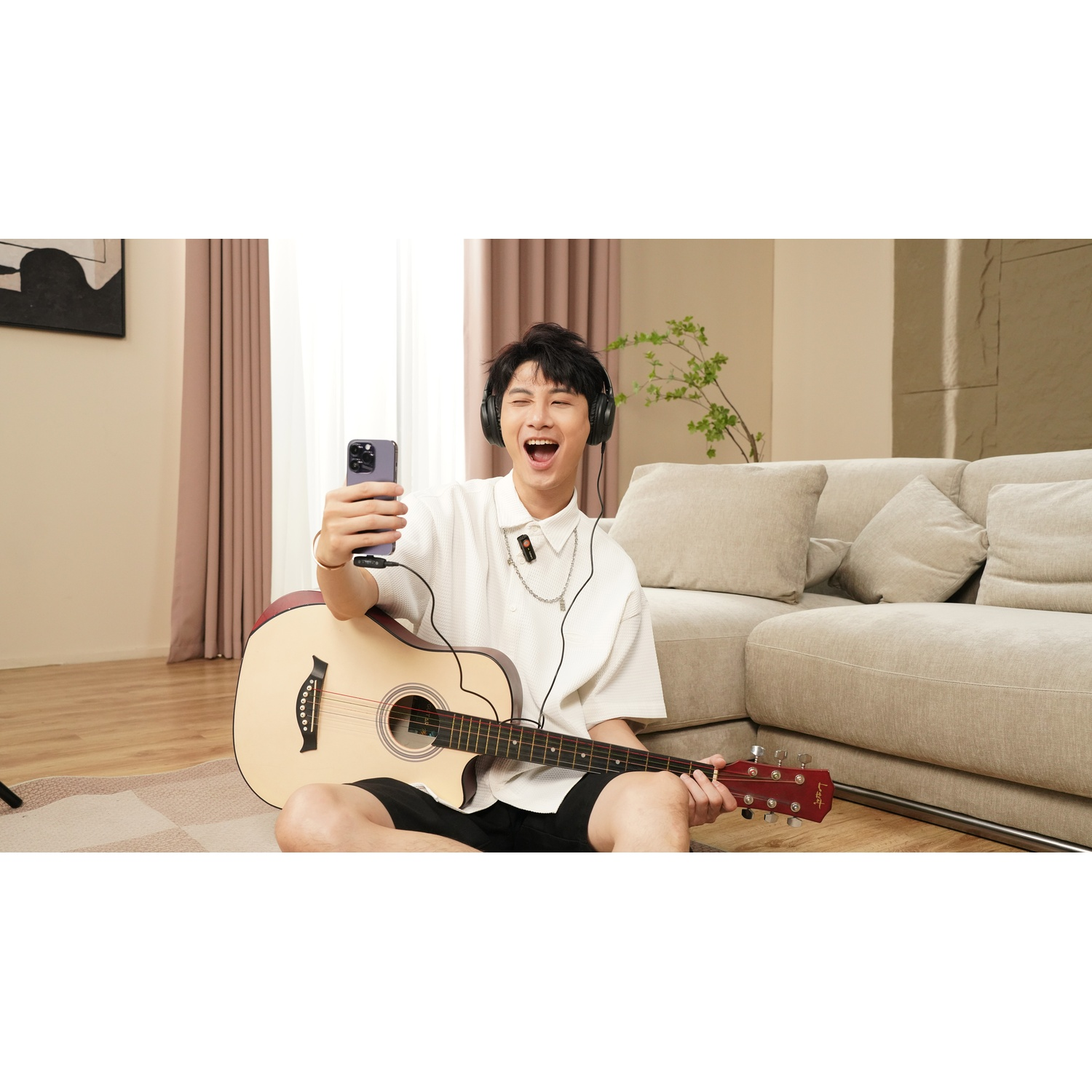Un uomo con cuffie suona la chitarra, tenendo un telefono per un selfie.