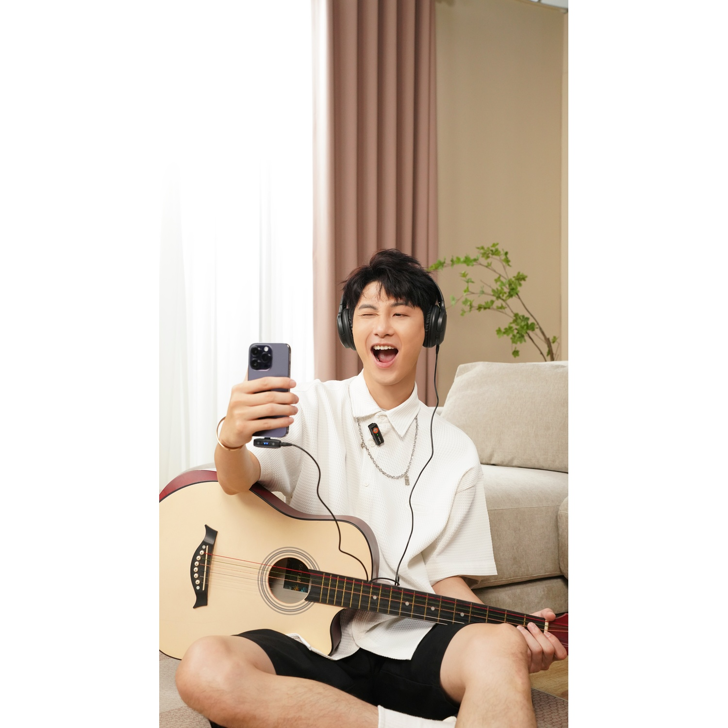 Un giovane con cuffie suona la chitarra e tiene un telefono.