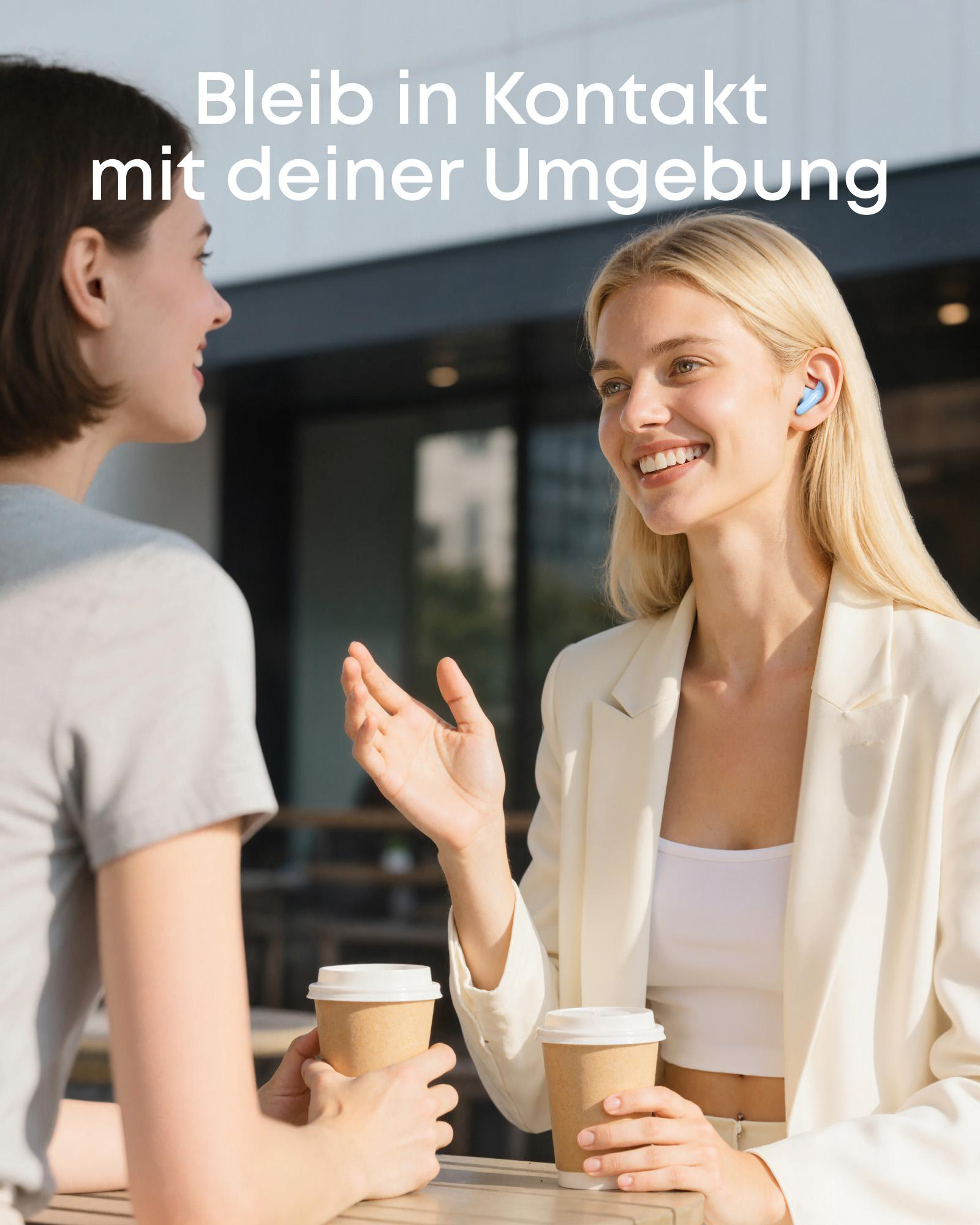 Zwei Frauen reden draußen, eine trägt blaue Ohrhörer und hält Kaffee.