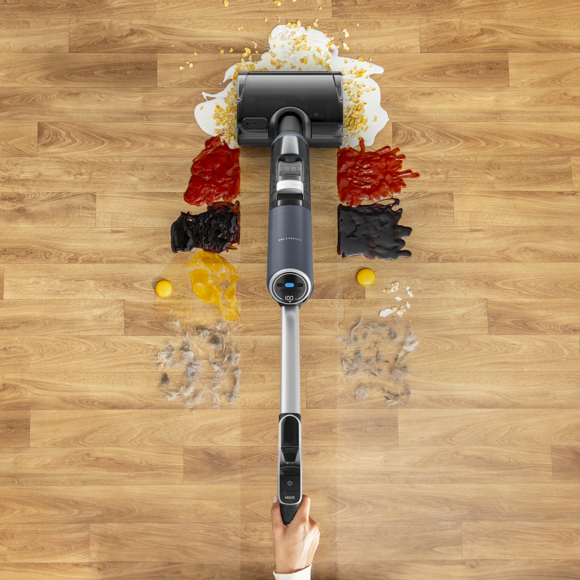 Un aspirateur à main nettoie de la nourriture renversée et des poils sur un plancher.