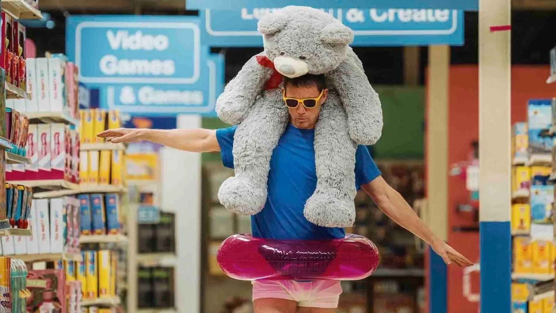 Mann mit Teddybär auf Schultern, der durch einen Spielzeugladen geht.