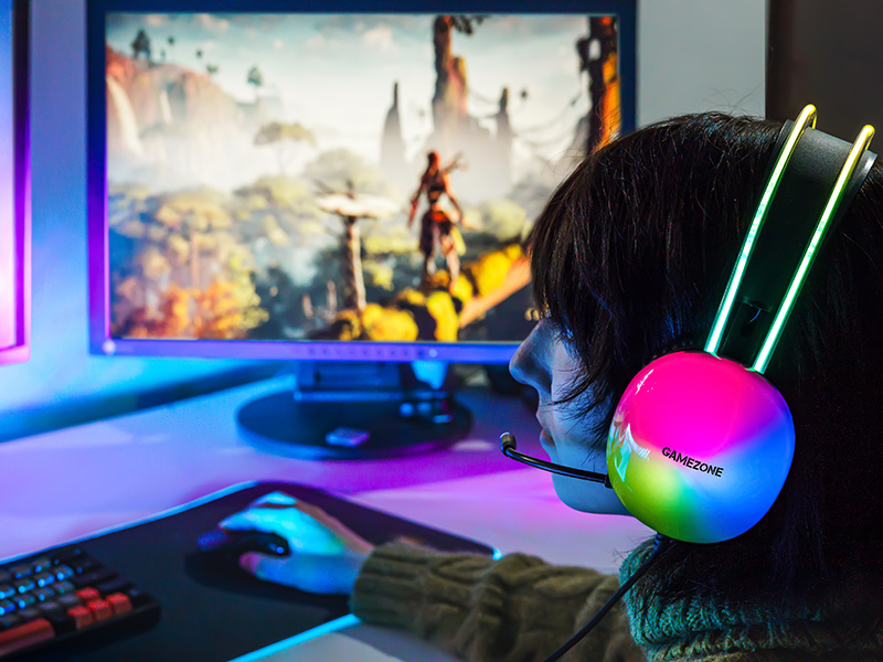 Osoba w kolorowych słuchawkach gamingowych gra w grę wideo na monitorze.