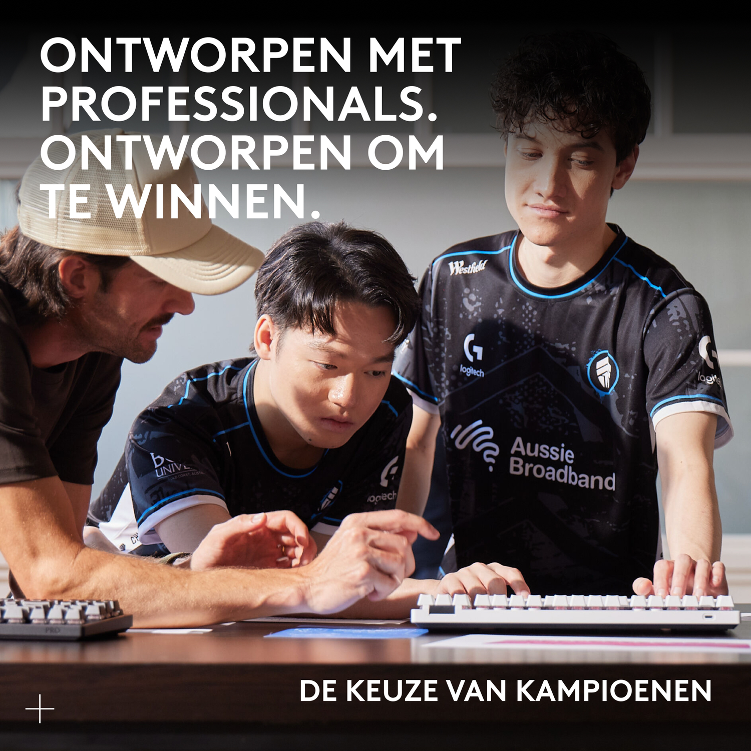 Three men at a desk, two playing esports, one watching.