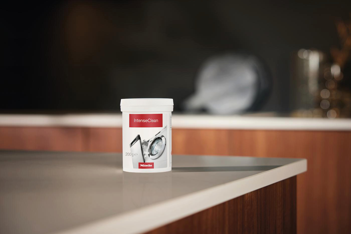 Ein weißer Behälter mit Miele IntenseClean Waschmaschinenreiniger steht auf einer Arbeitsplatte.
