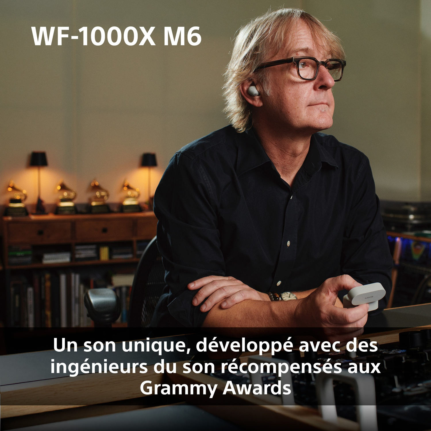 Homme avec lunettes porte des écouteurs blancs. Grammys sur étagère.