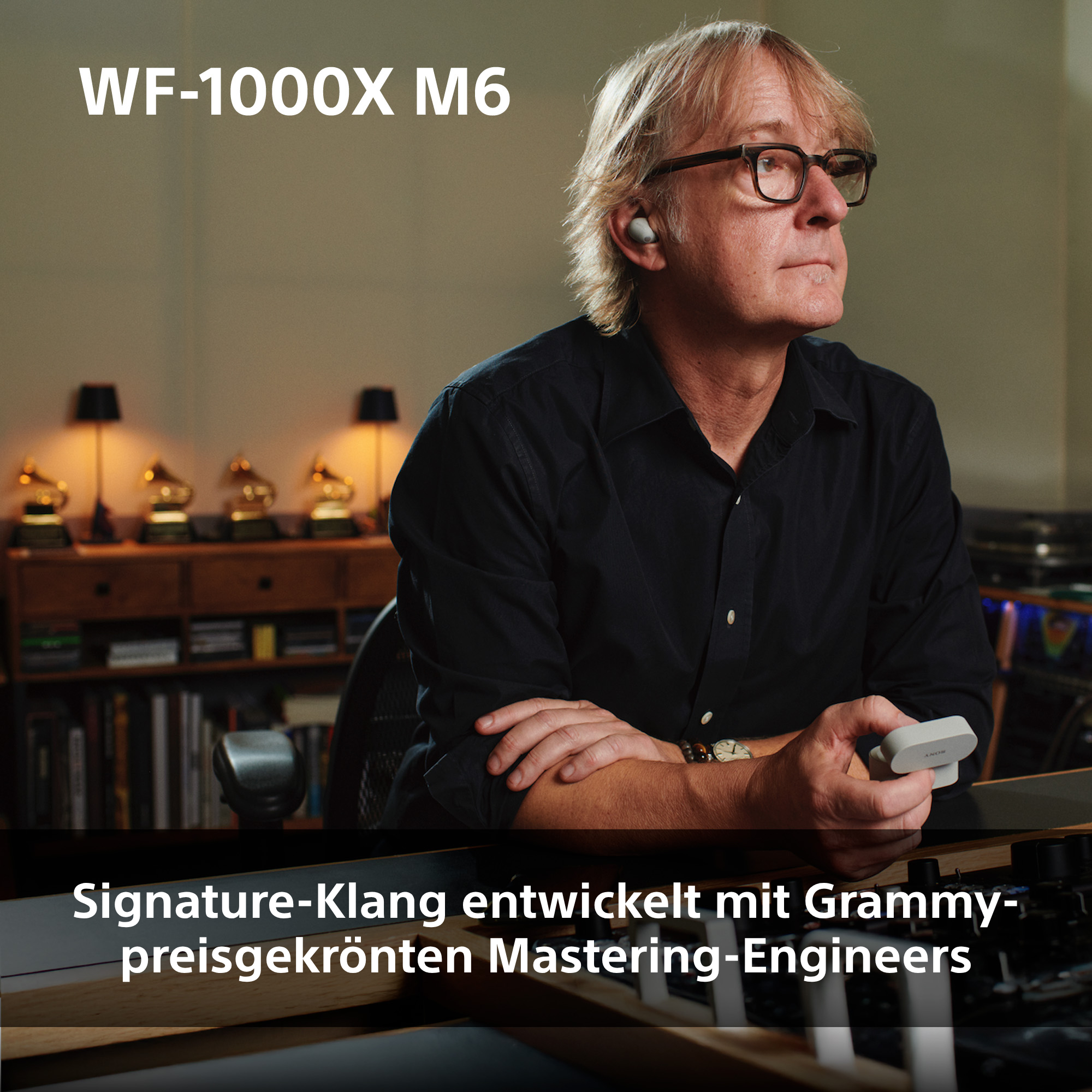 Mann mit Brille und Ohrhörer hält Ladecase, im Hintergrund Grammys.