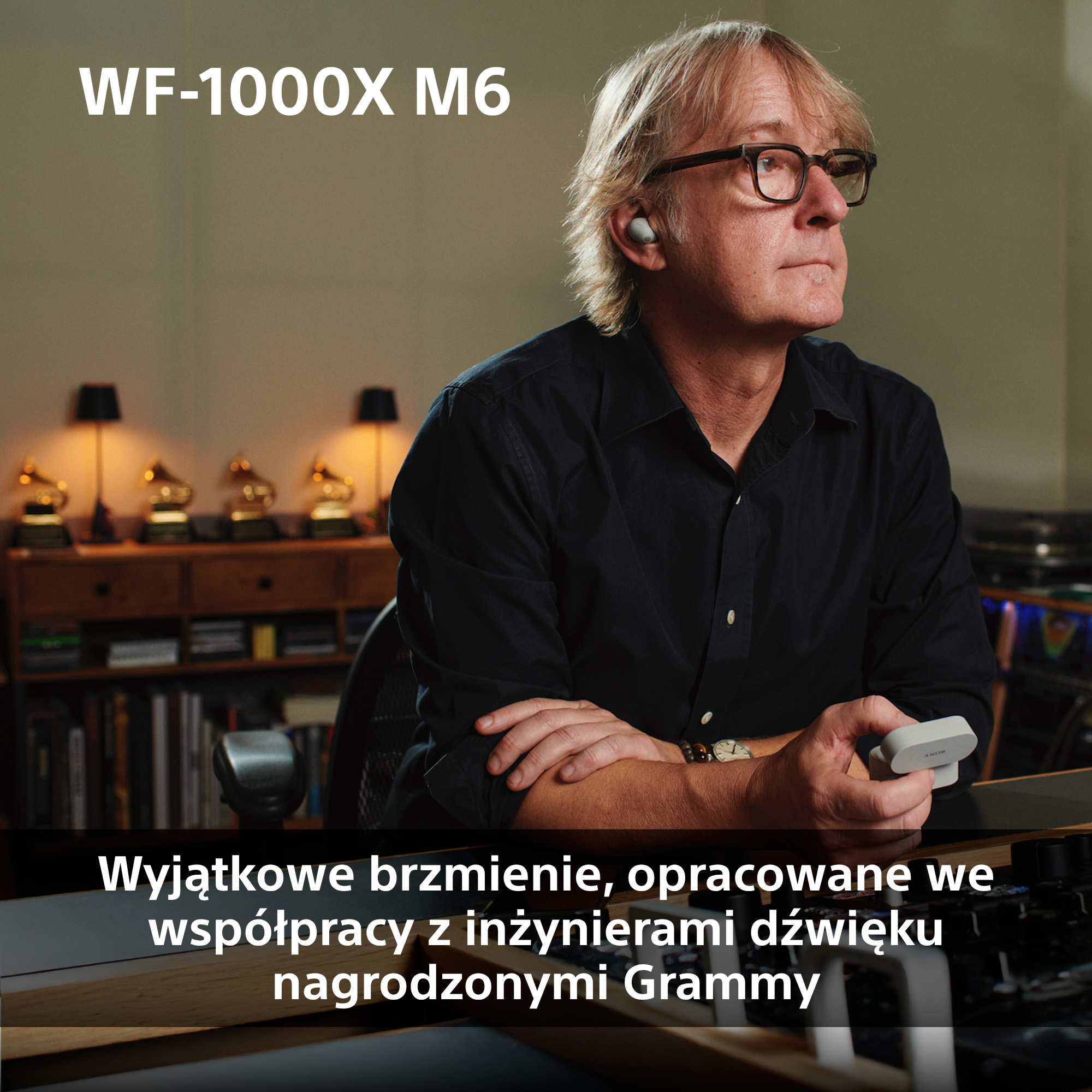 Mężczyzna w okularach i słuchawką trzyma etui ładujące. Trophies Grammy w tle.