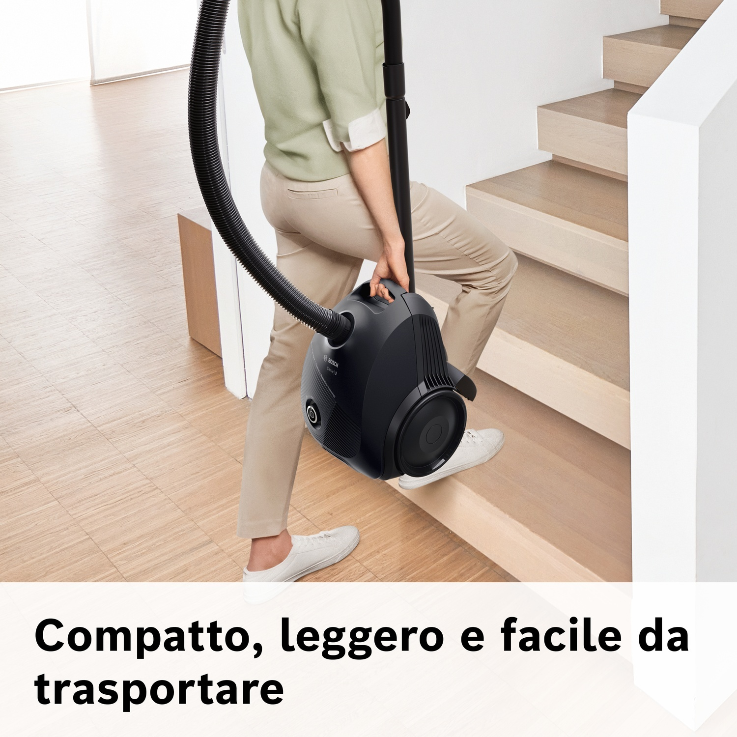 Una persona porta un aspirapolvere Bosch nero su una scala di legno.