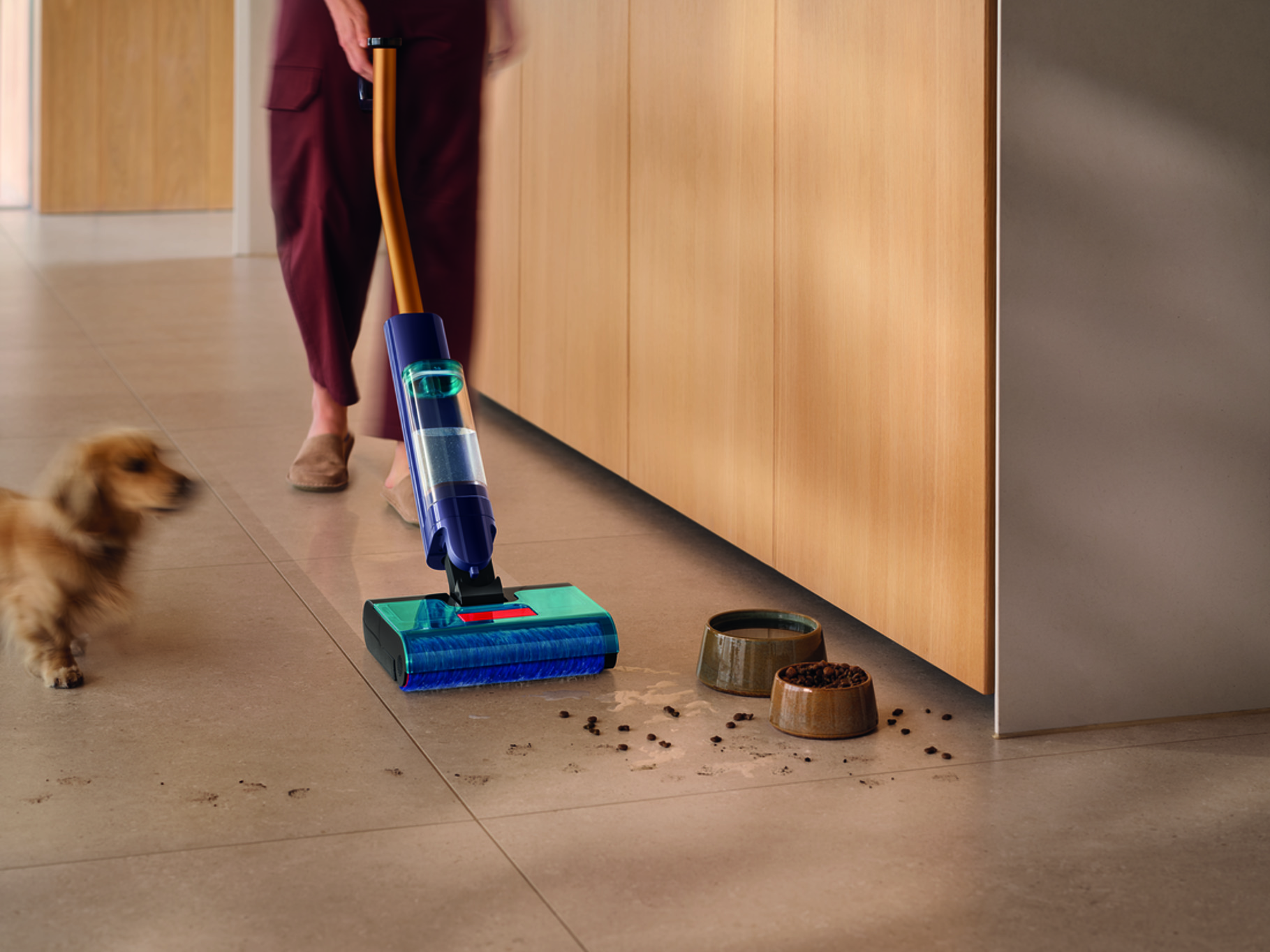 Pies i odkurzacz na kafelkowym podłodze z miskami dla zwierząt.