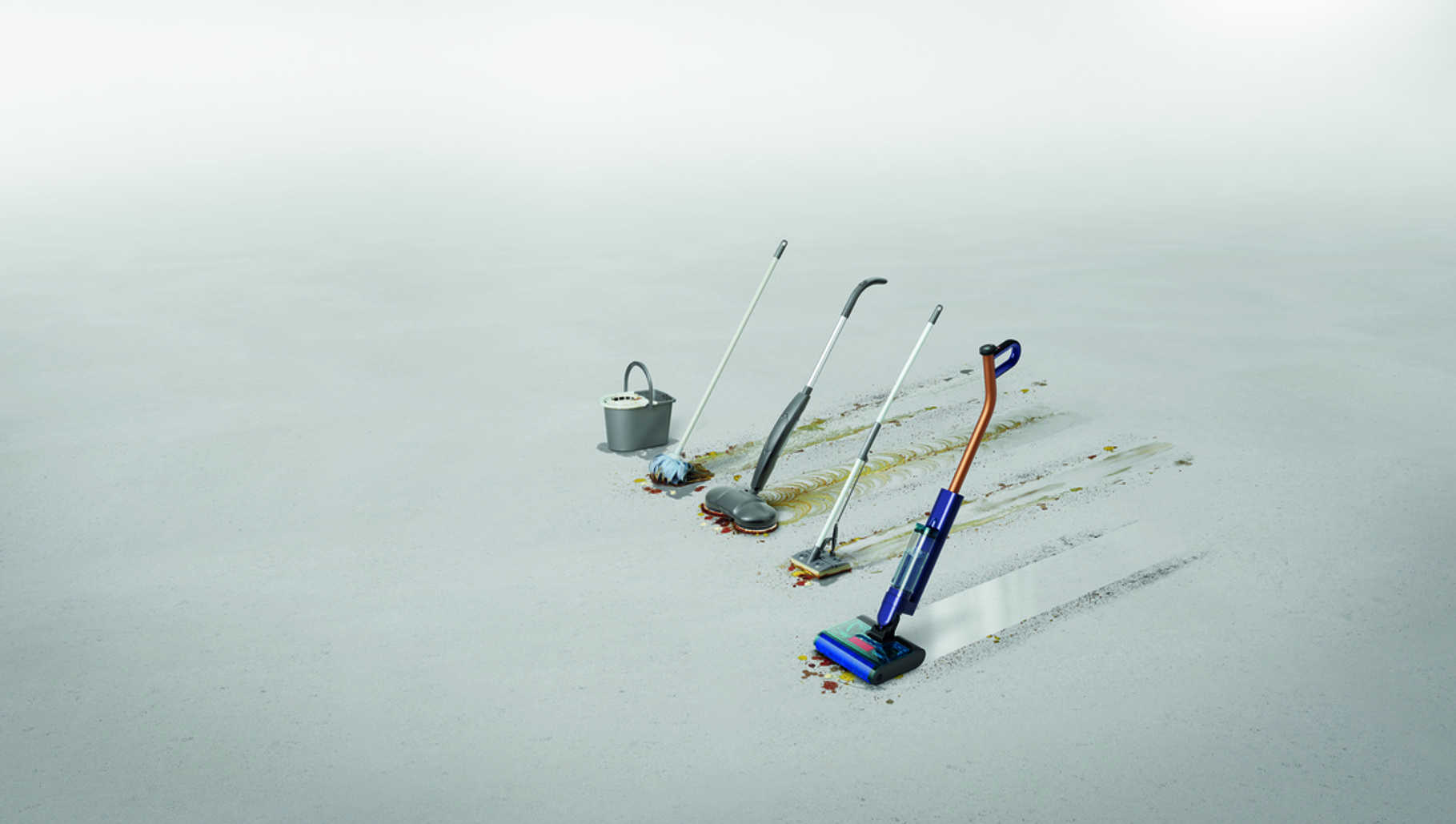 Cztery przyrządy do czyszczenia na szarej podłodze ze śladami brudu.