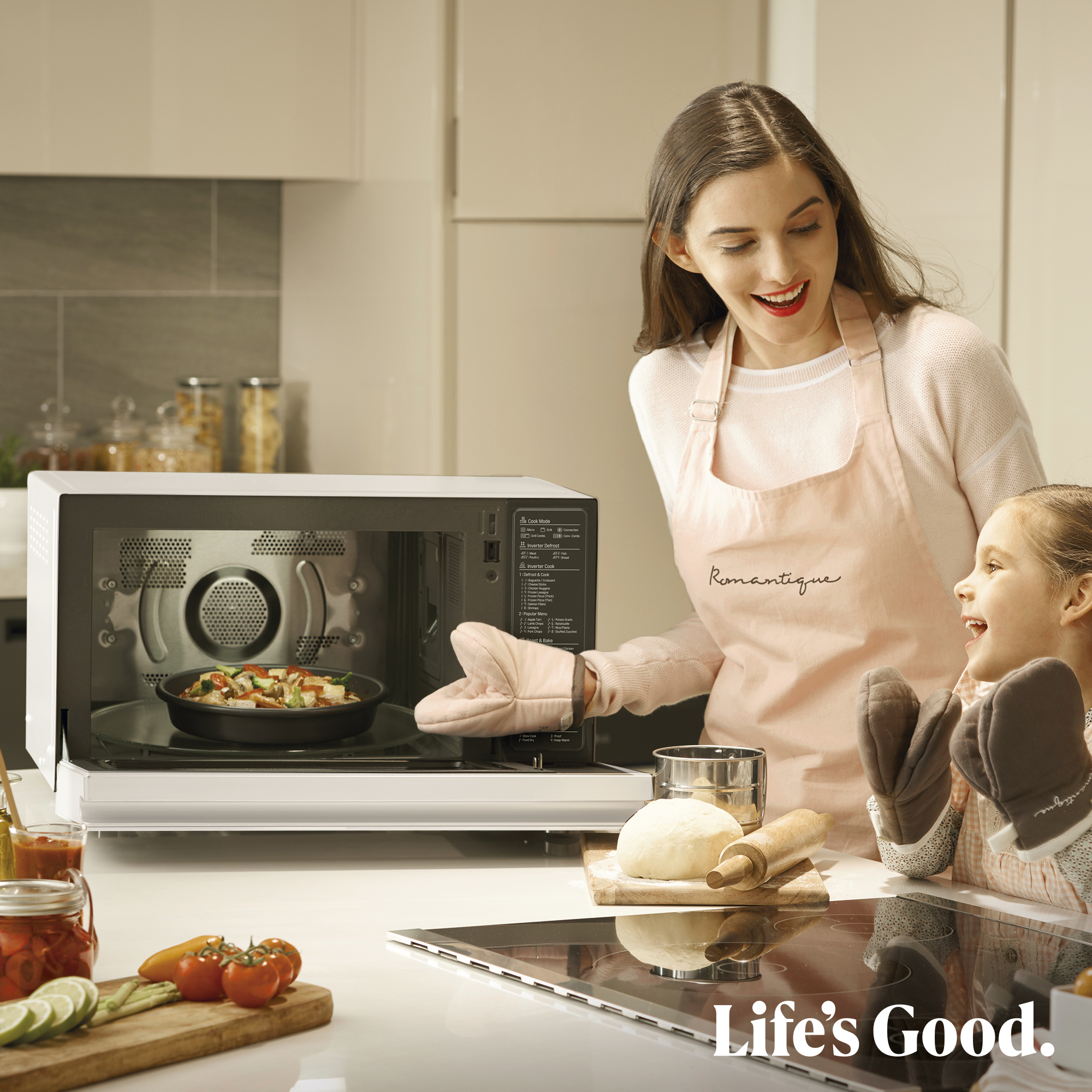 Una mujer y un niño en una cocina con un microondas abierto, comida dentro.