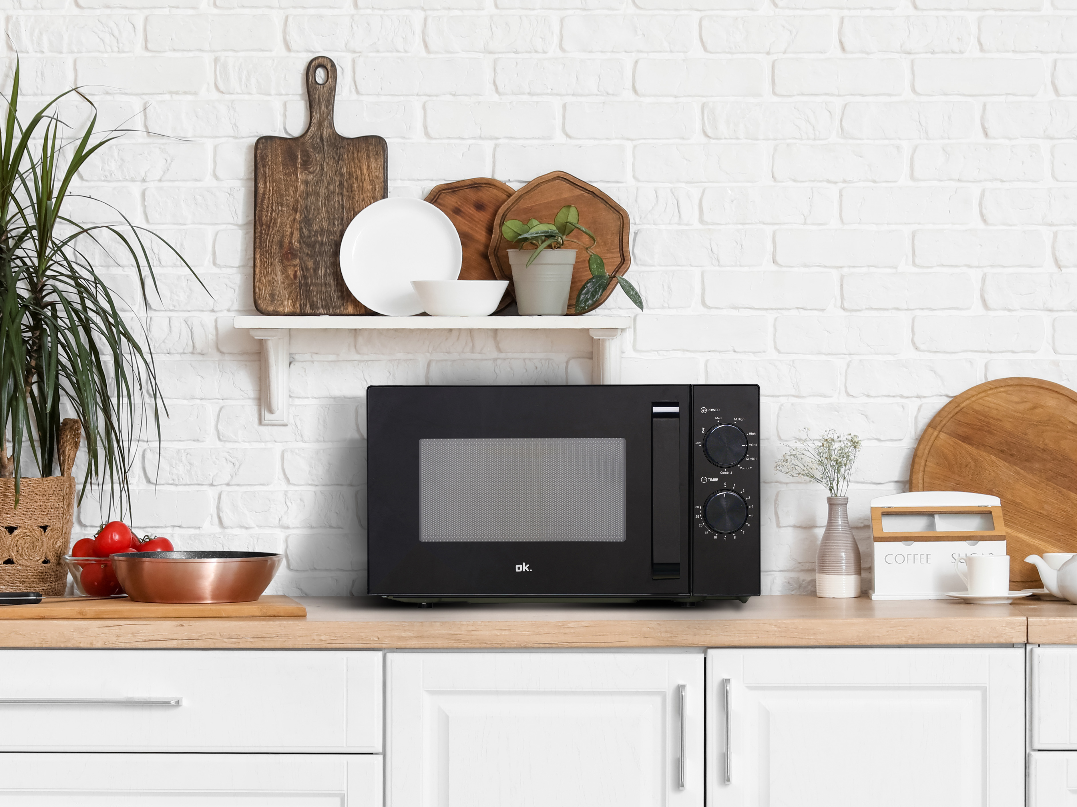 Czarna kuchenka mikrofalowa na blacie kuchennym z białym ceglanym murem w tle.