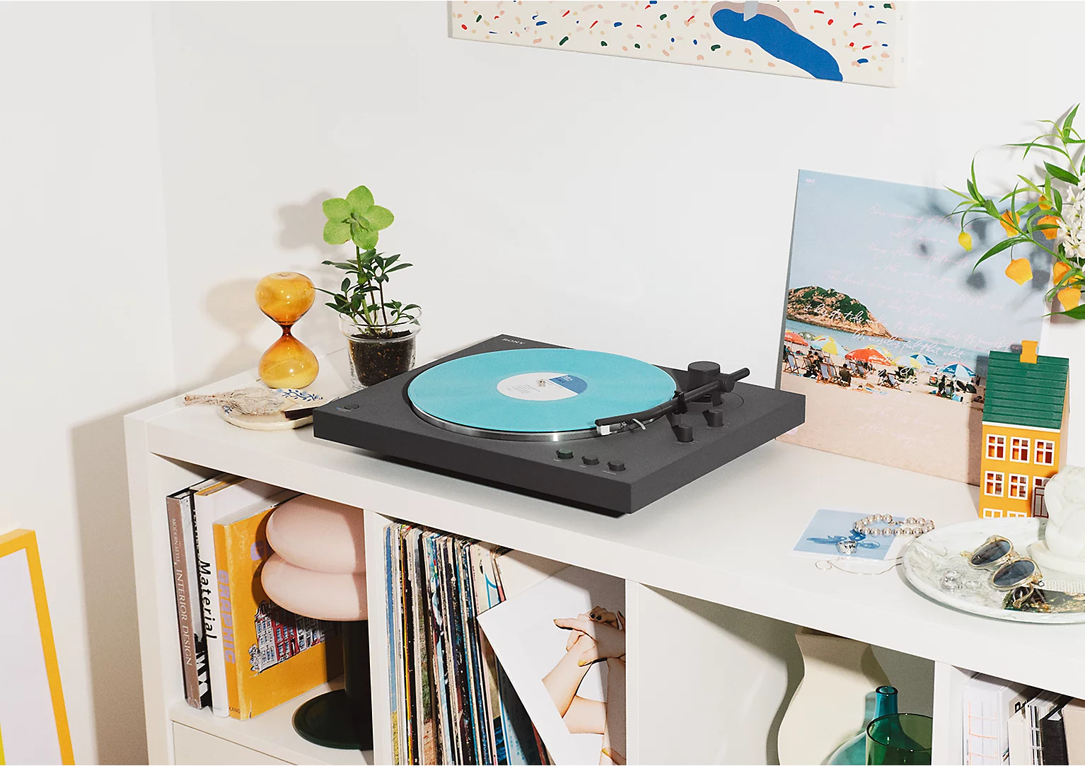 Gramofon z niebieską płytą stoi na półce z dekoracjami.