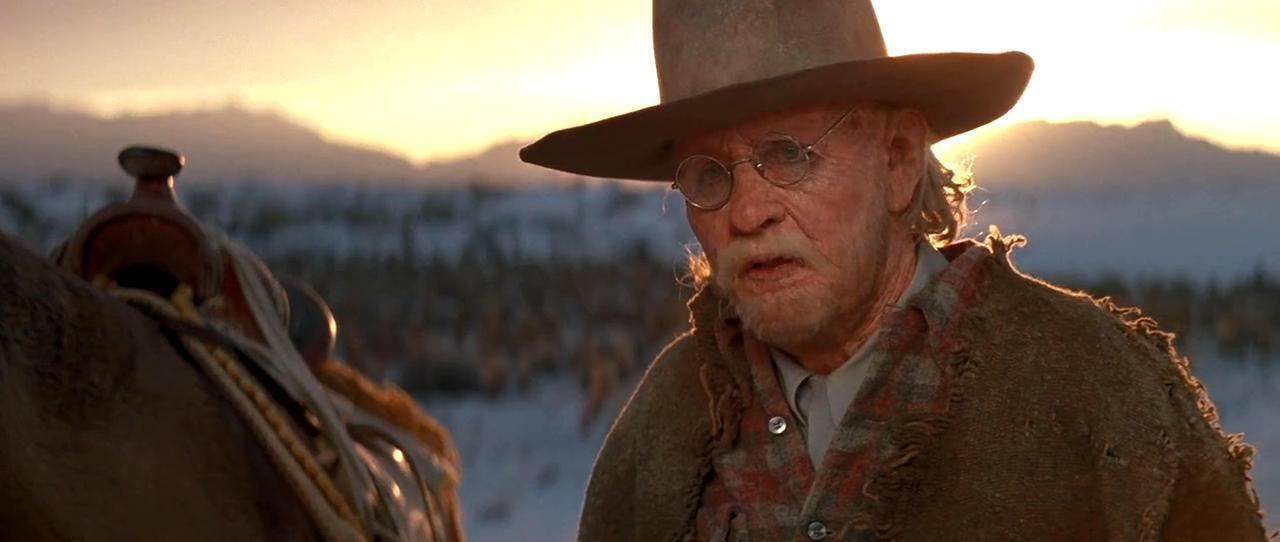 Älterer Mann mit Hut und Brille reitet auf einem Pferd im Sonnenuntergang.