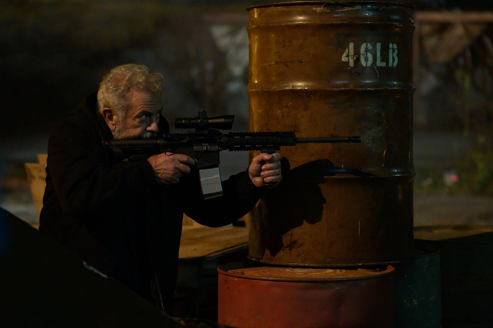 Mann mit Gewehr zielt auf ein rostiges Fass mit der Aufschrift 46LB.