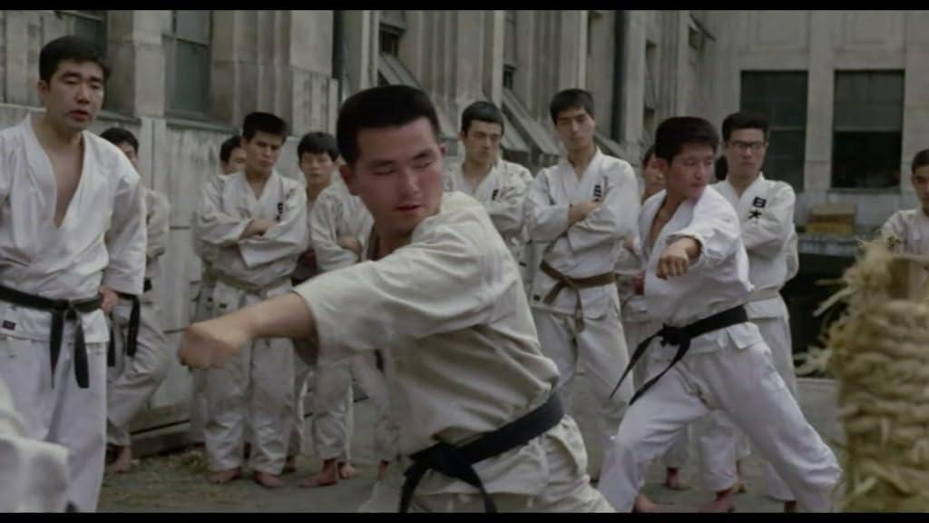 Männer in weißen Karate-Anzügen üben Schläge vor einem Gebäude.