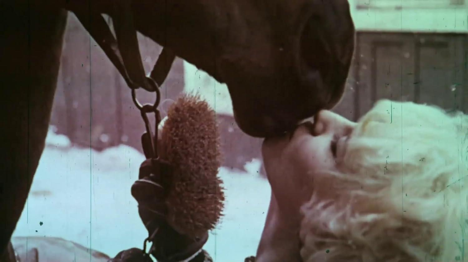 Eine Frau mit blonden Haaren küsst ein Pferd im Winter.