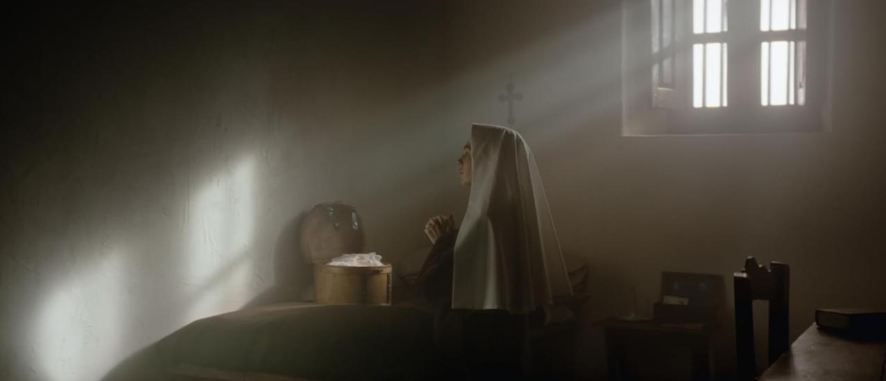 Eine Nonne in weißem Habit betet in einem Raum, der von Sonnenlicht durchflutet wird.