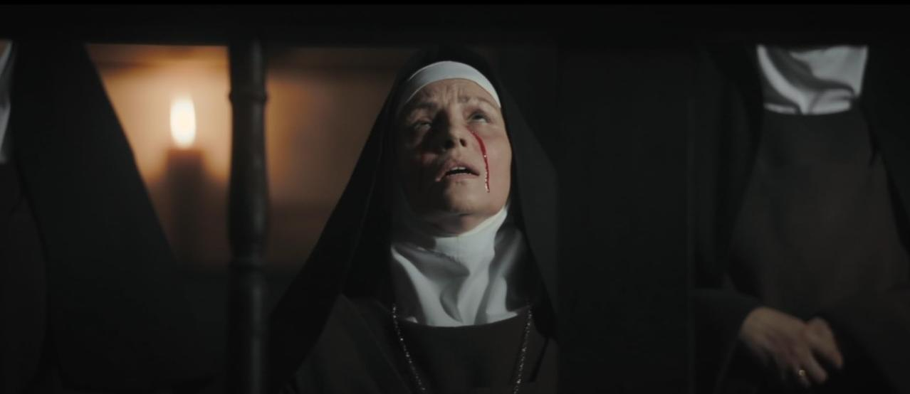 Eine Nonne mit blutigen Wunden blickt nach oben, Kerzenlicht im Hintergrund.