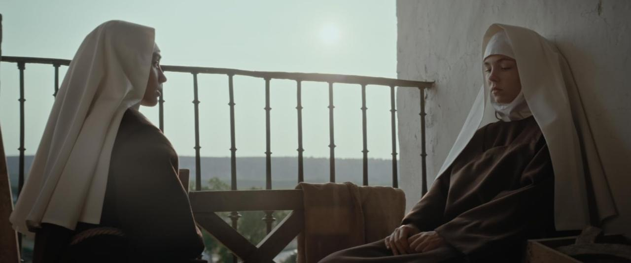Zwei Nonnen in braunen Kutten und weißen Schleiern sitzen auf einer Veranda im Sonnenlicht.