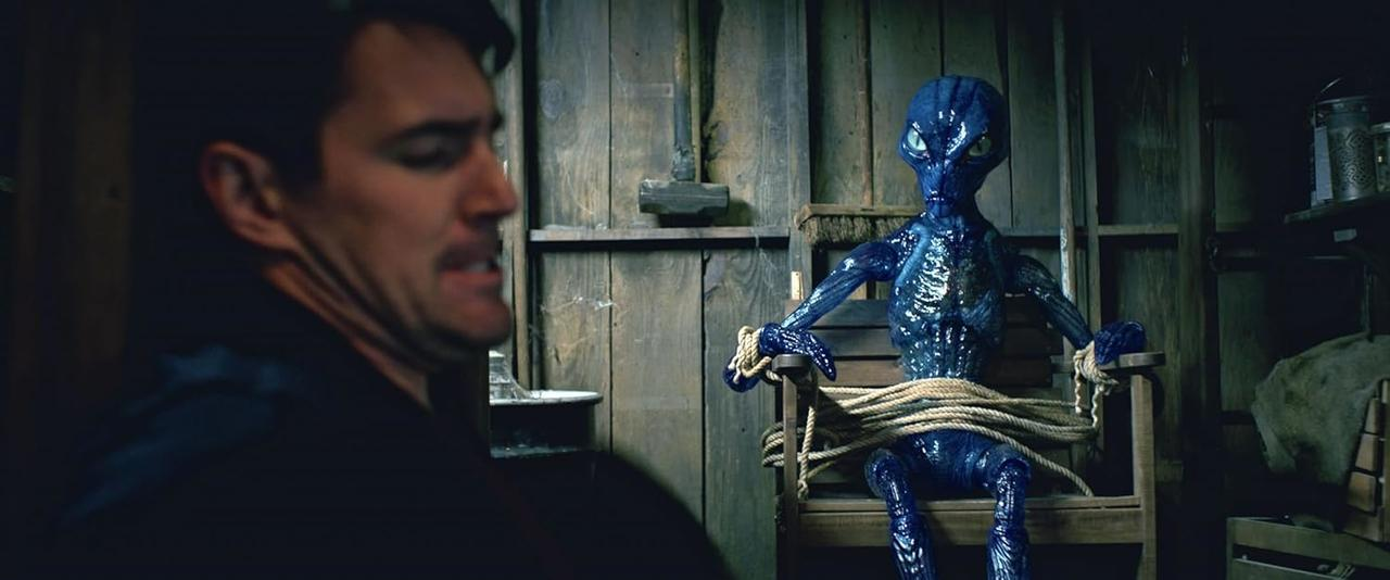 Ein blauer Alien ist gefesselt auf einem Stuhl in einer Scheune.