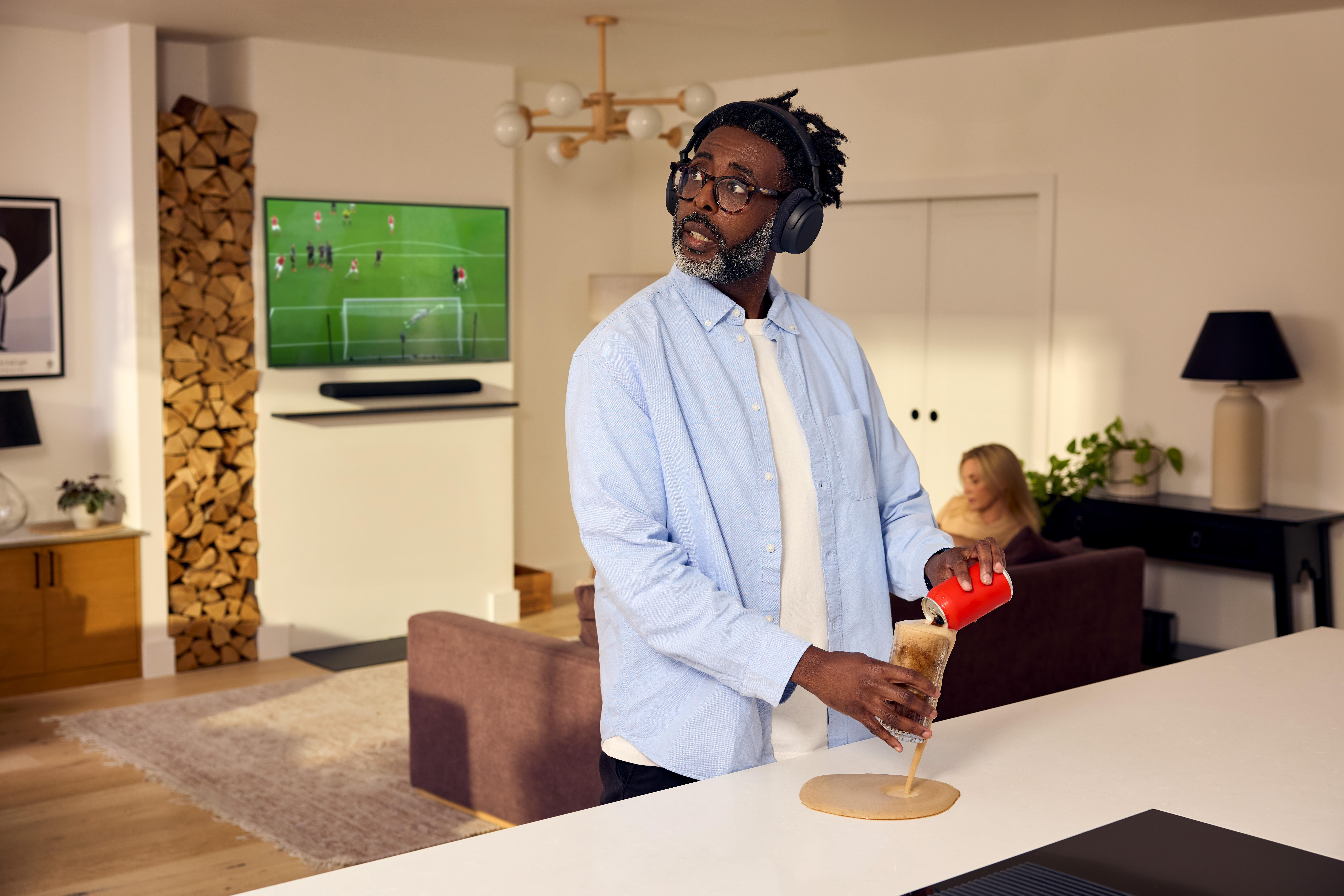 Mann mit Kopfhörern gießt Getränk über den Tisch, während Fußball läuft.