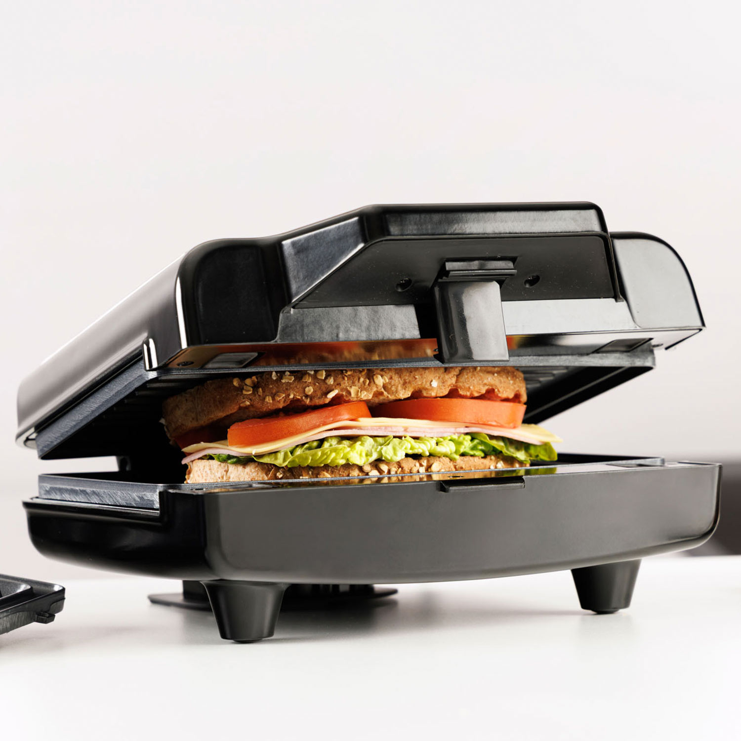 Un sándwich con pan, lechuga, tomate y queso en una sandwichera negra.