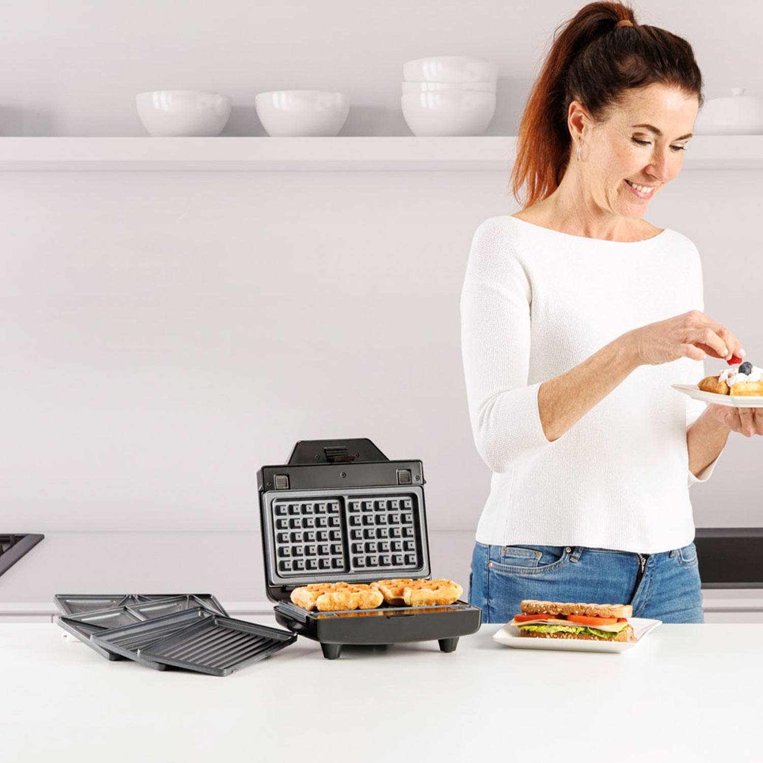 Mujer adornando gofres con bayas; sándwich y gofrera cerca.