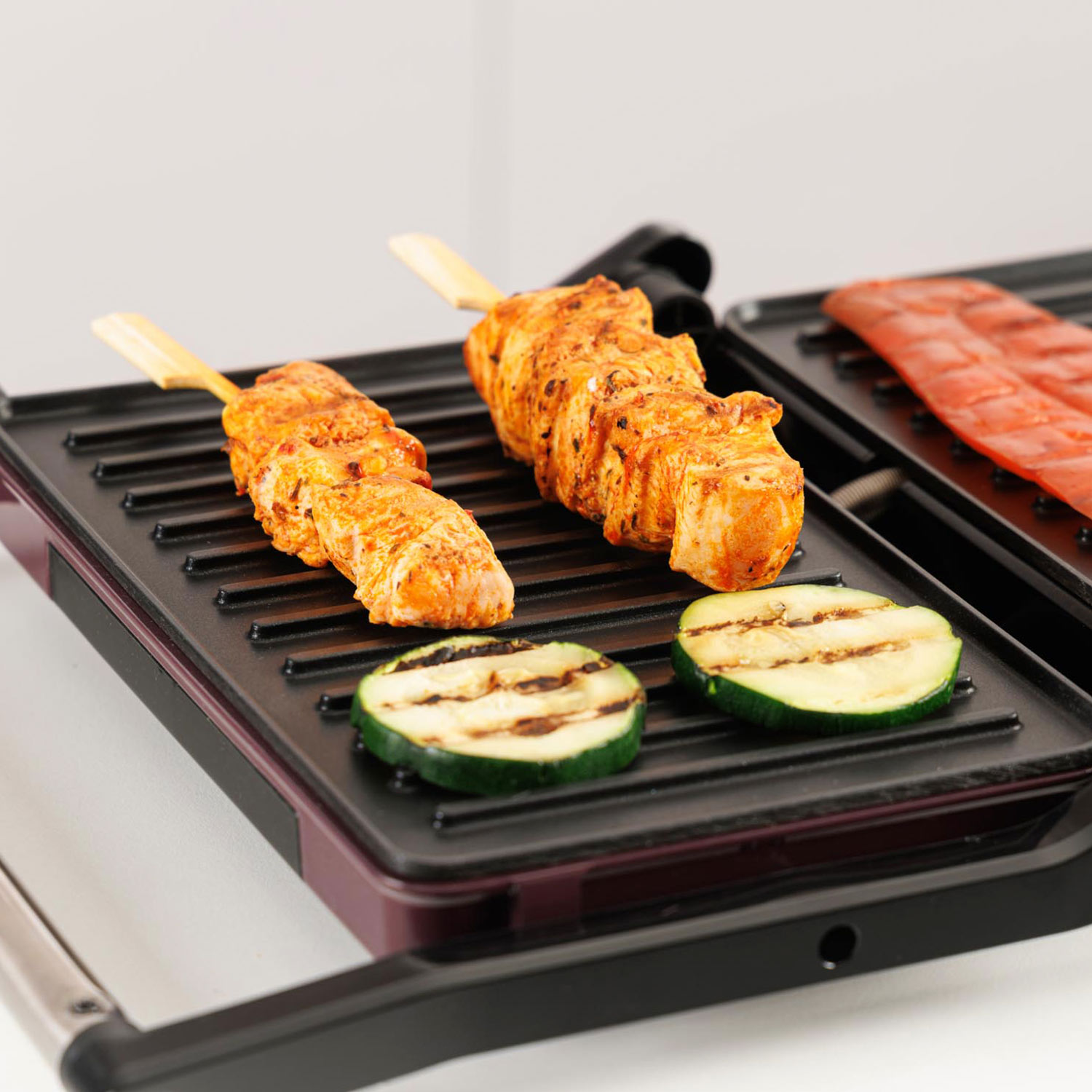 Brochetas de pollo y rodajas de calabacín en una parrilla.