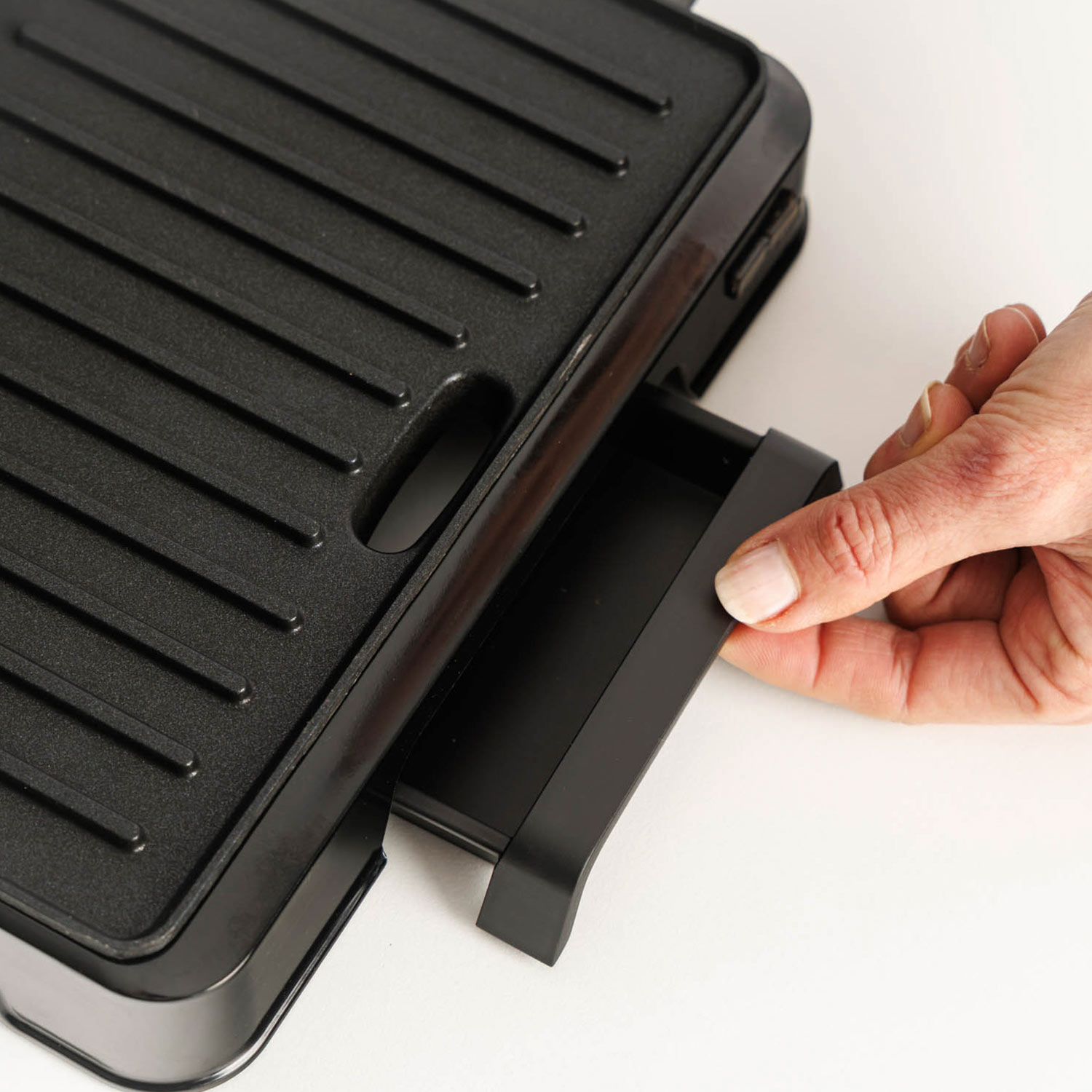 Mano saca un cajón de una parrilla negra.