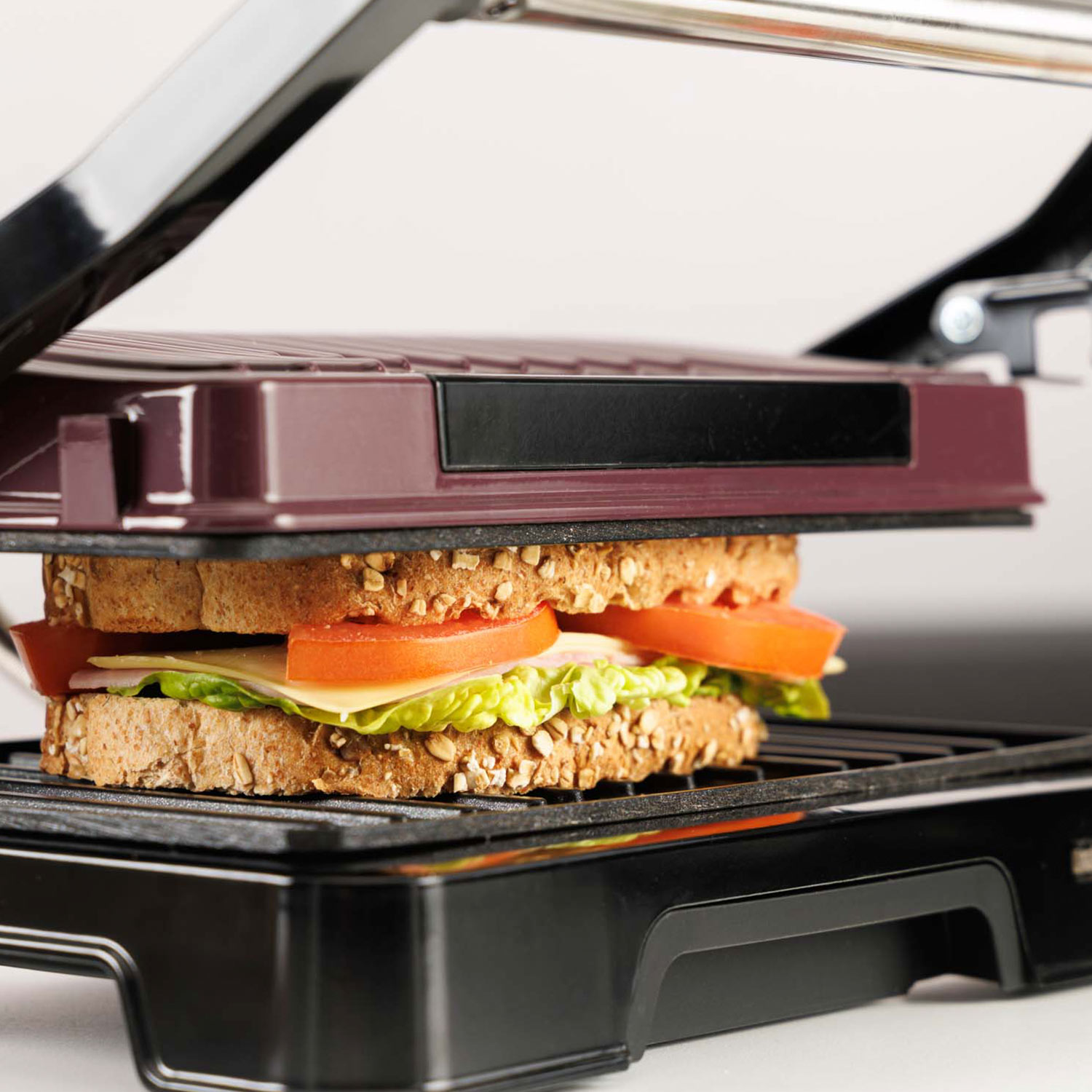 Un sándwich con pan tostado, queso, lechuga y tomate en una parrilla de contacto.