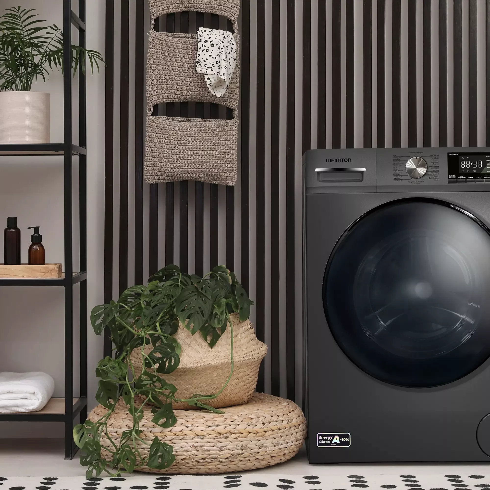 Lavadora gris oscuro junto a plantas y estanterías con toallas y jabón.