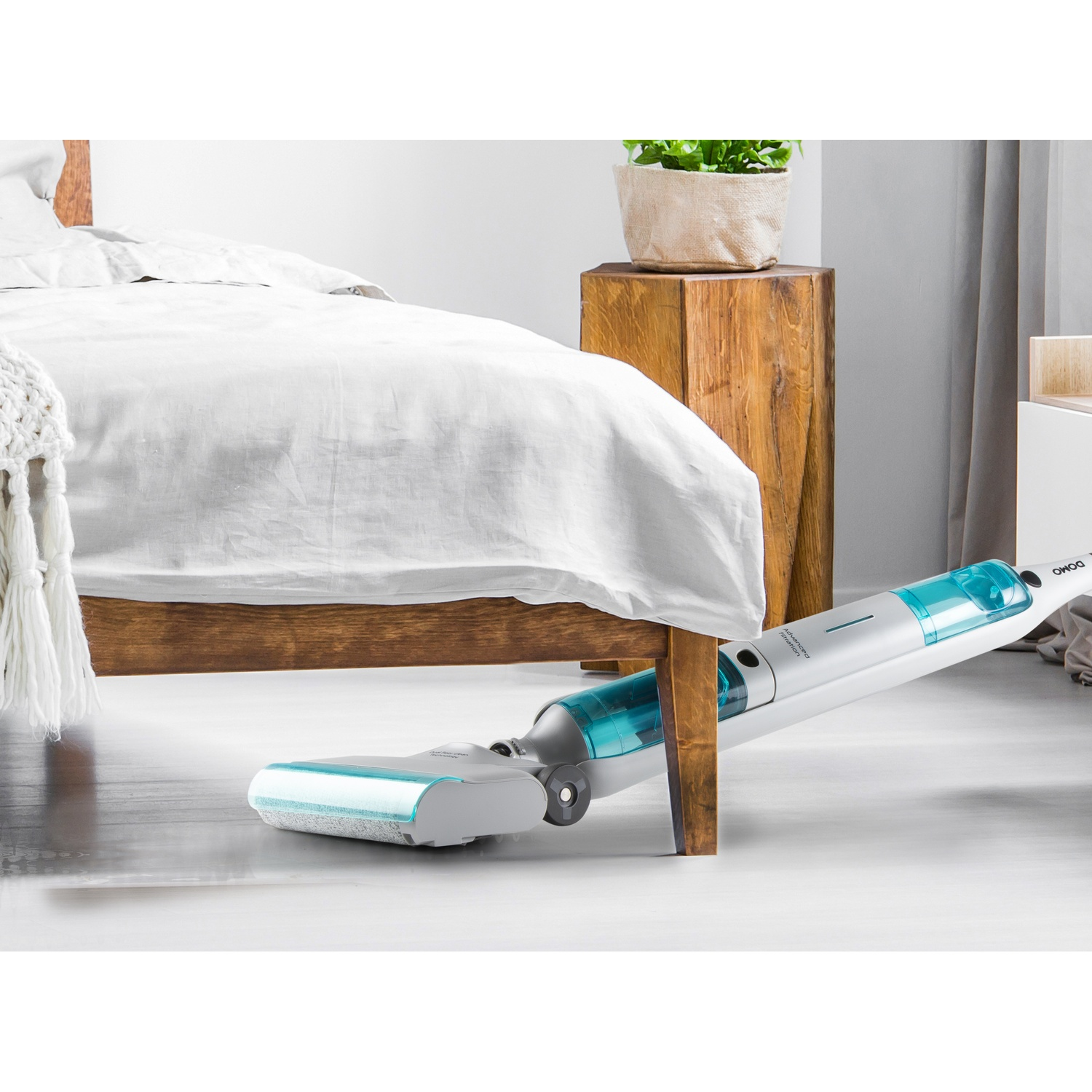 Un aspirateur sans fil blanc avec réservoir bleu sous un lit en bois.