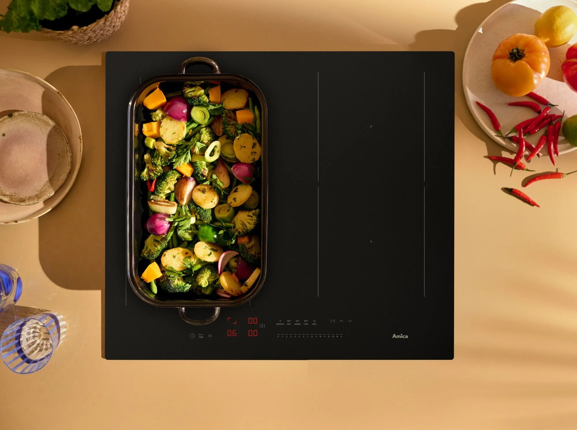 Płyta grzewcza z naczyniem żaroodpornym pełnym pieczonych warzyw i owoców.