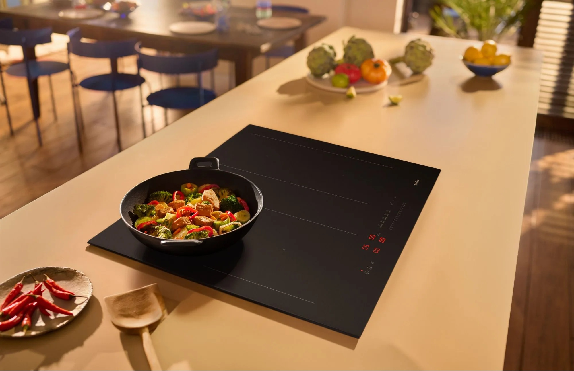 Wok z kurczakiem i warzywami na płycie indukcyjnej z papryczkami chili obok.