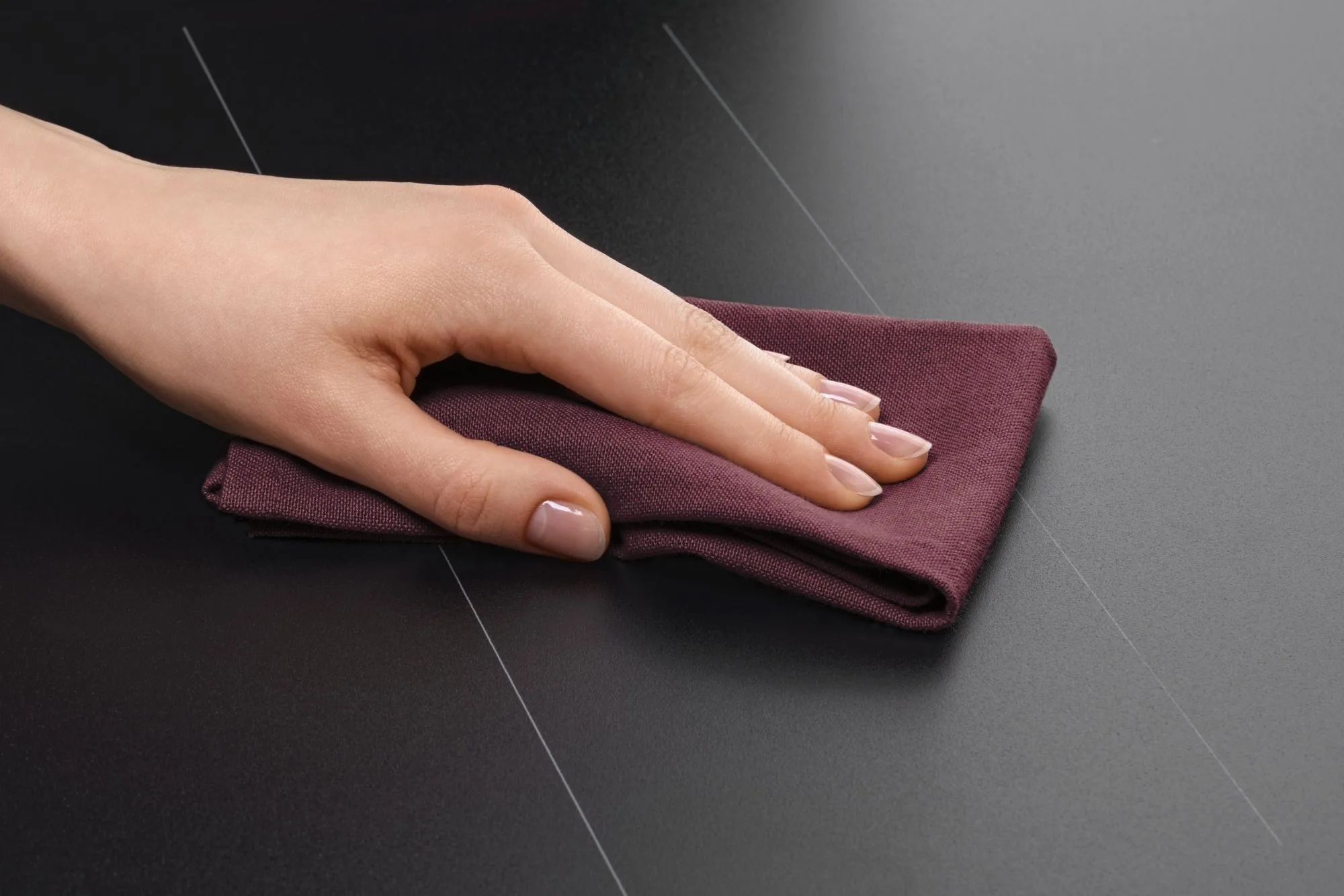 Dłoń przeciera ciemną powierzchnię ściereczką.