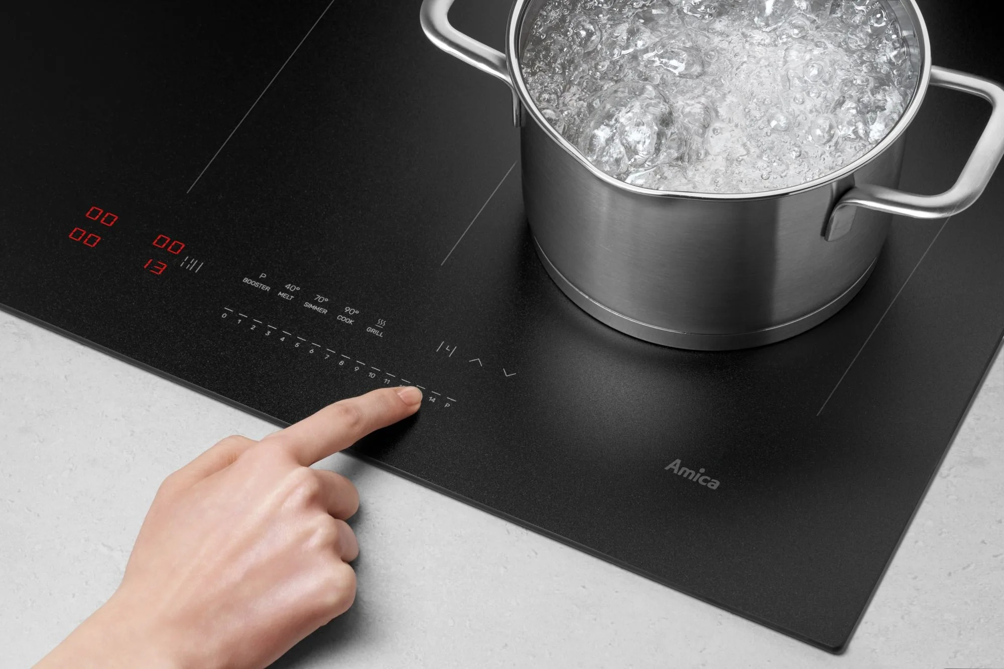 Dłoń dotyka płyty indukcyjnej, podczas gdy woda gotuje się w garnku.
