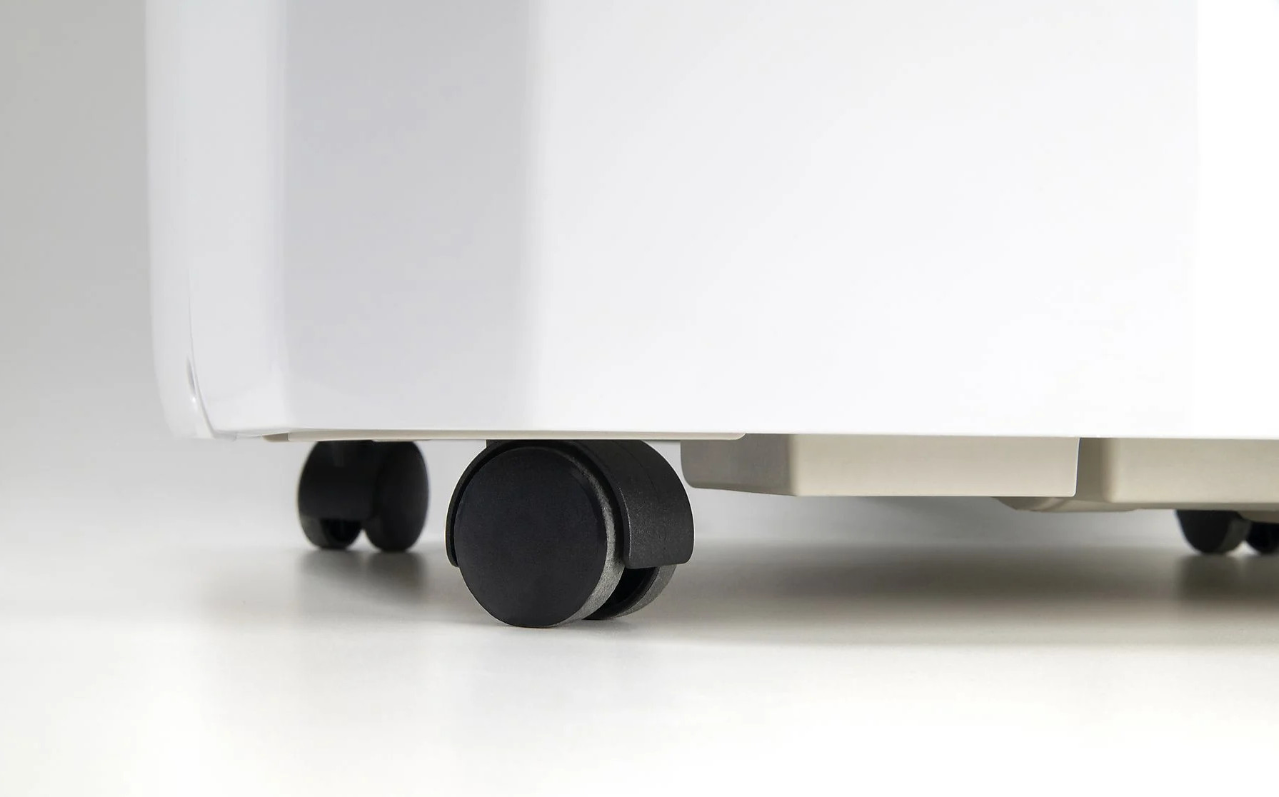 Zbliżenie czterech czarnych kółek u dołu białego urządzenia na białej powierzchni.